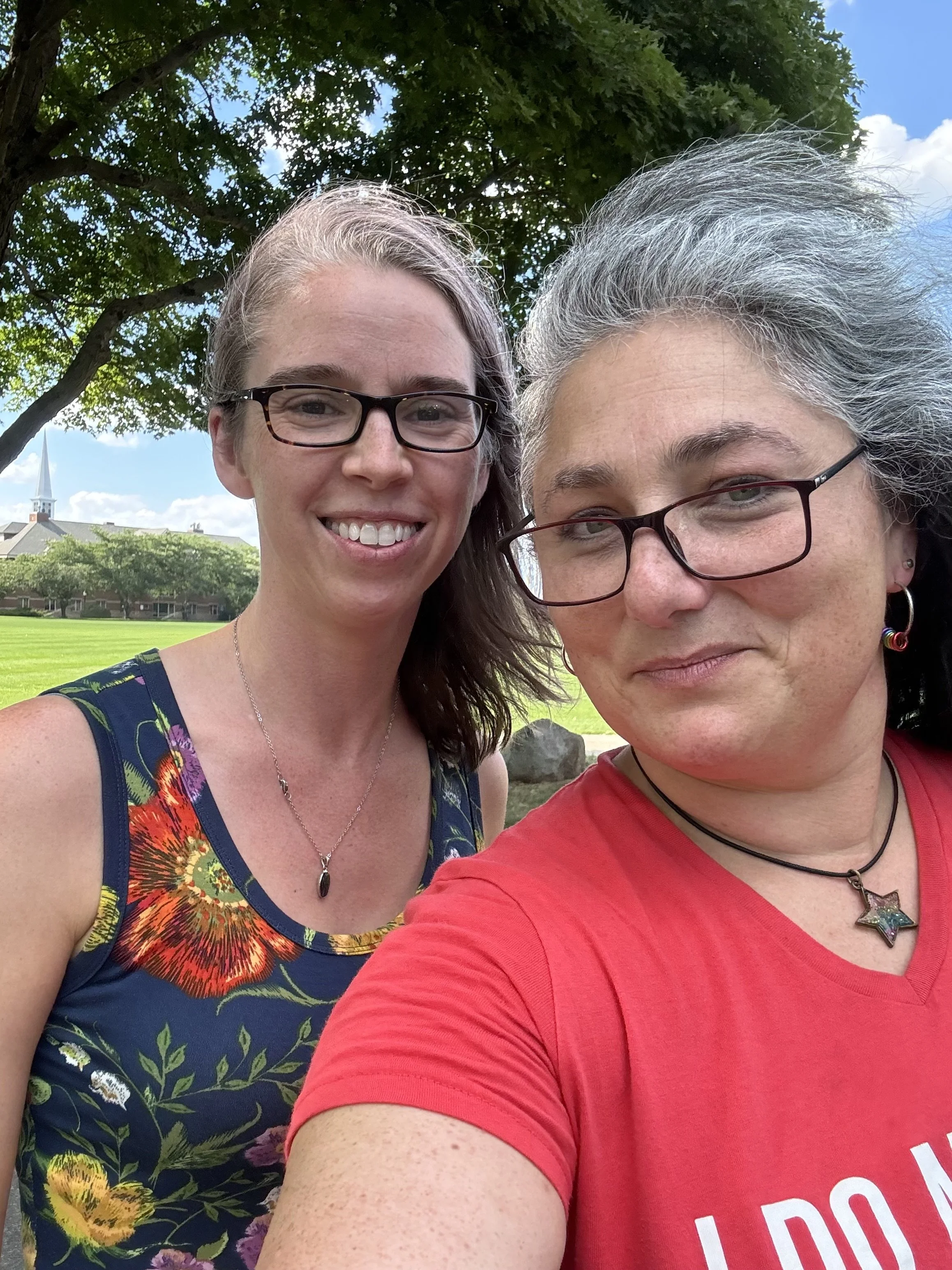 Two white women with grey hair, glasses and pendant necklaces pose for a smiling selfie.