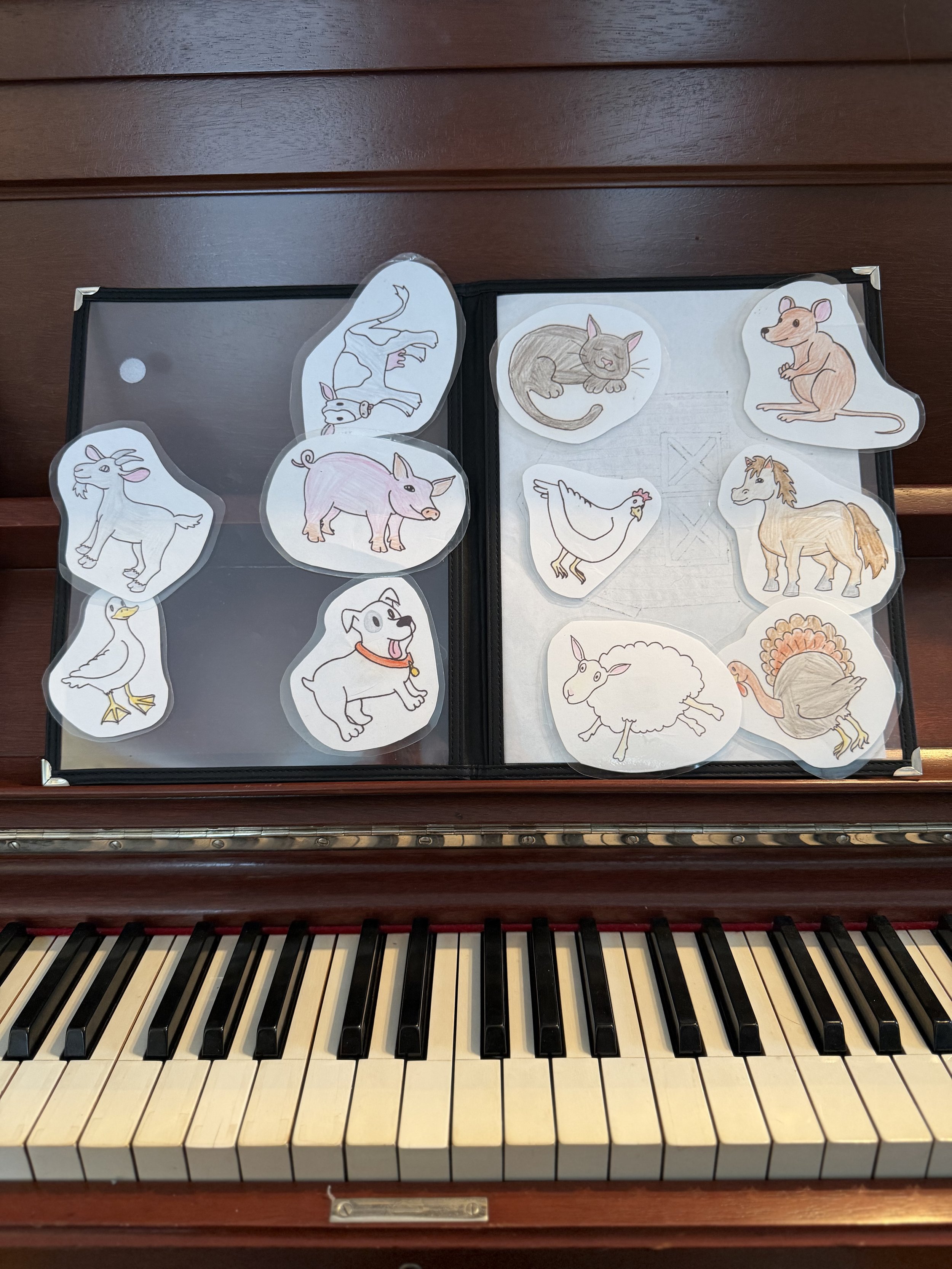 A two-page velcro board sitting on a piano displays hand drawn farm animal choices.