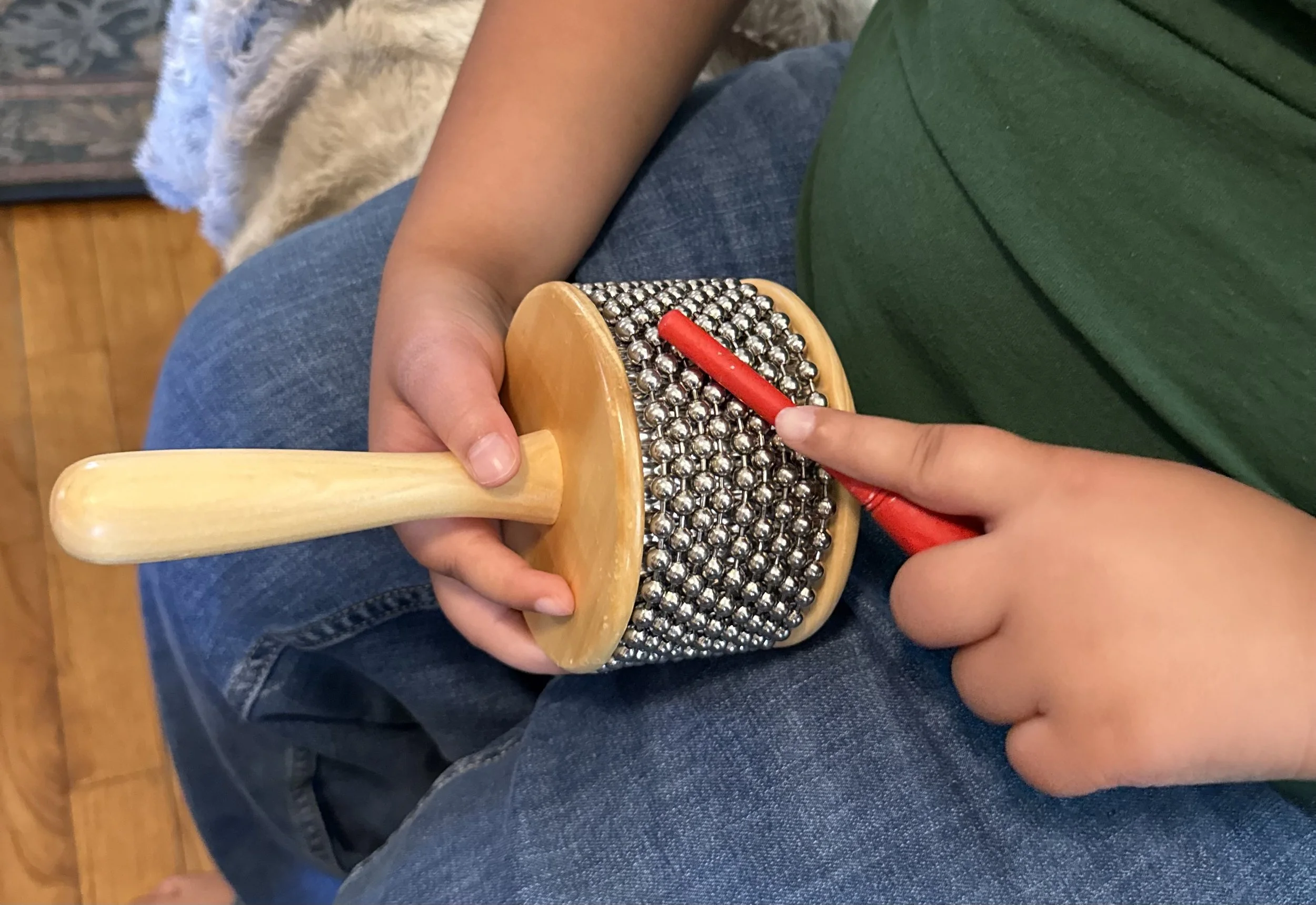 The hands of a child wearing a green shirt hold a cabasa percussion instrument and a stick-like striker