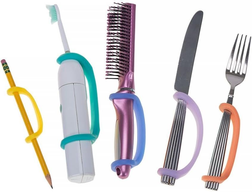 A collection of colorful toothbrushes, a yellow pencil, a vibrating toothbrush, a purple hairbrush, a small knife, and a fork with silicone grip assists attached to the handles.