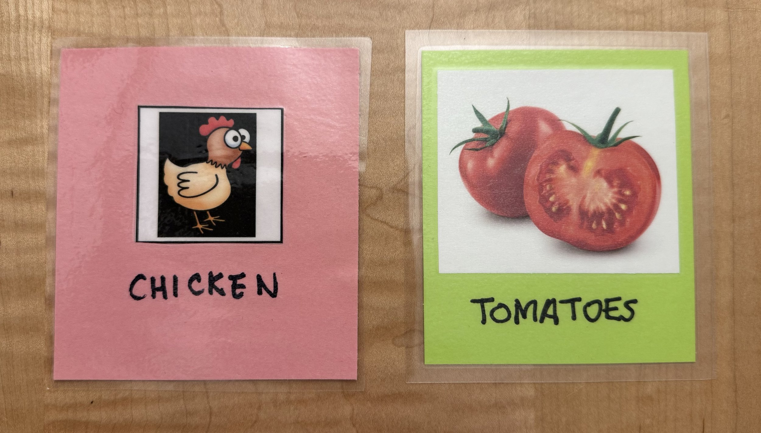 Two choice cards are displayed on a wooden background. On the left is a pick card with a small cartoon chicken. On the right is a neon green card with a photo of tomatoes. Both images are labeled in black marker.