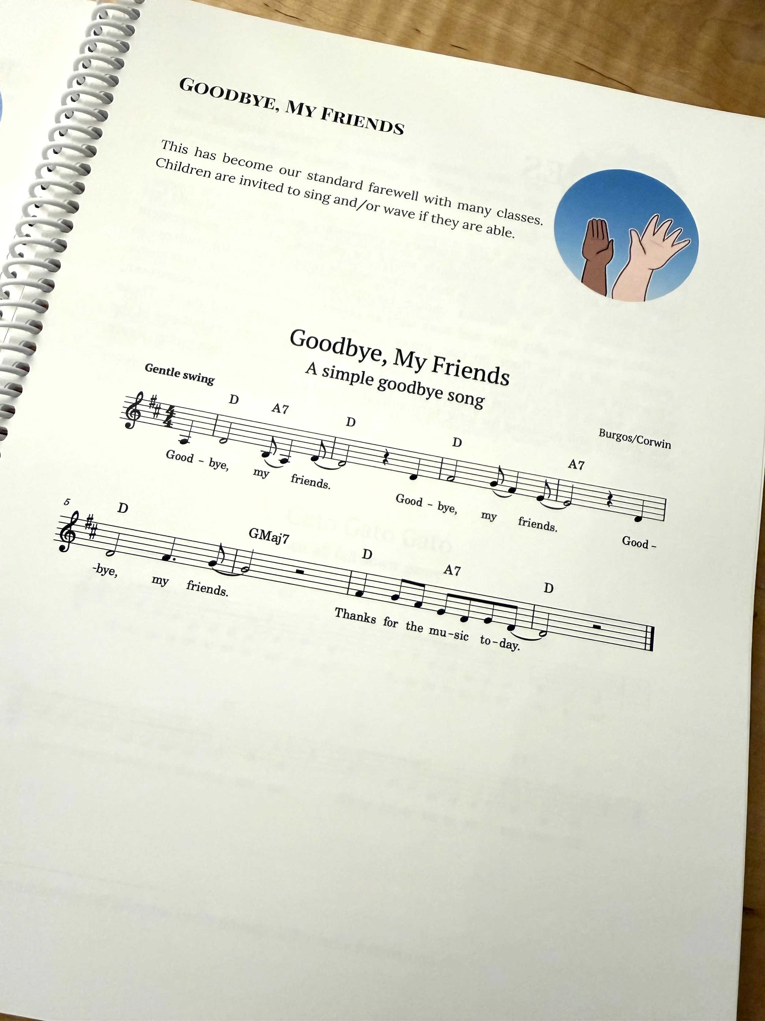 A page from a songbook shows a song called Goodbye, My Friends in Western classical music notation. The page includes a cartoon icon of two waving hands in contrasting skin tones on a blue gradient circle.