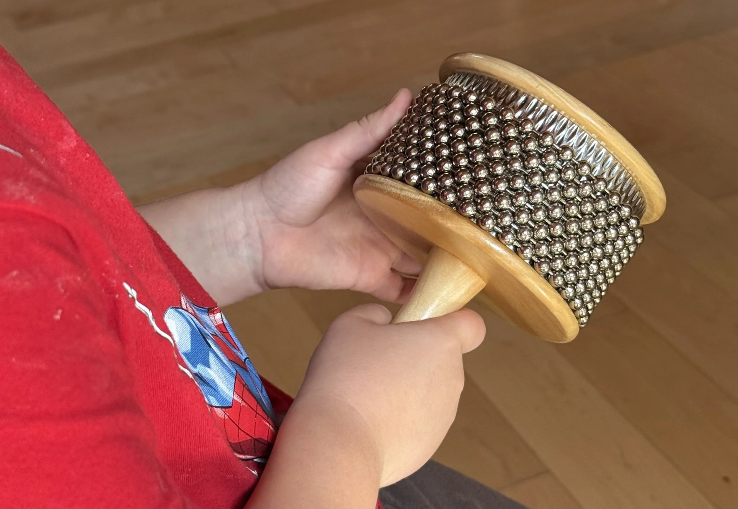 The hands of a child wearing a red shirt play with a cabasa percussion instrument.