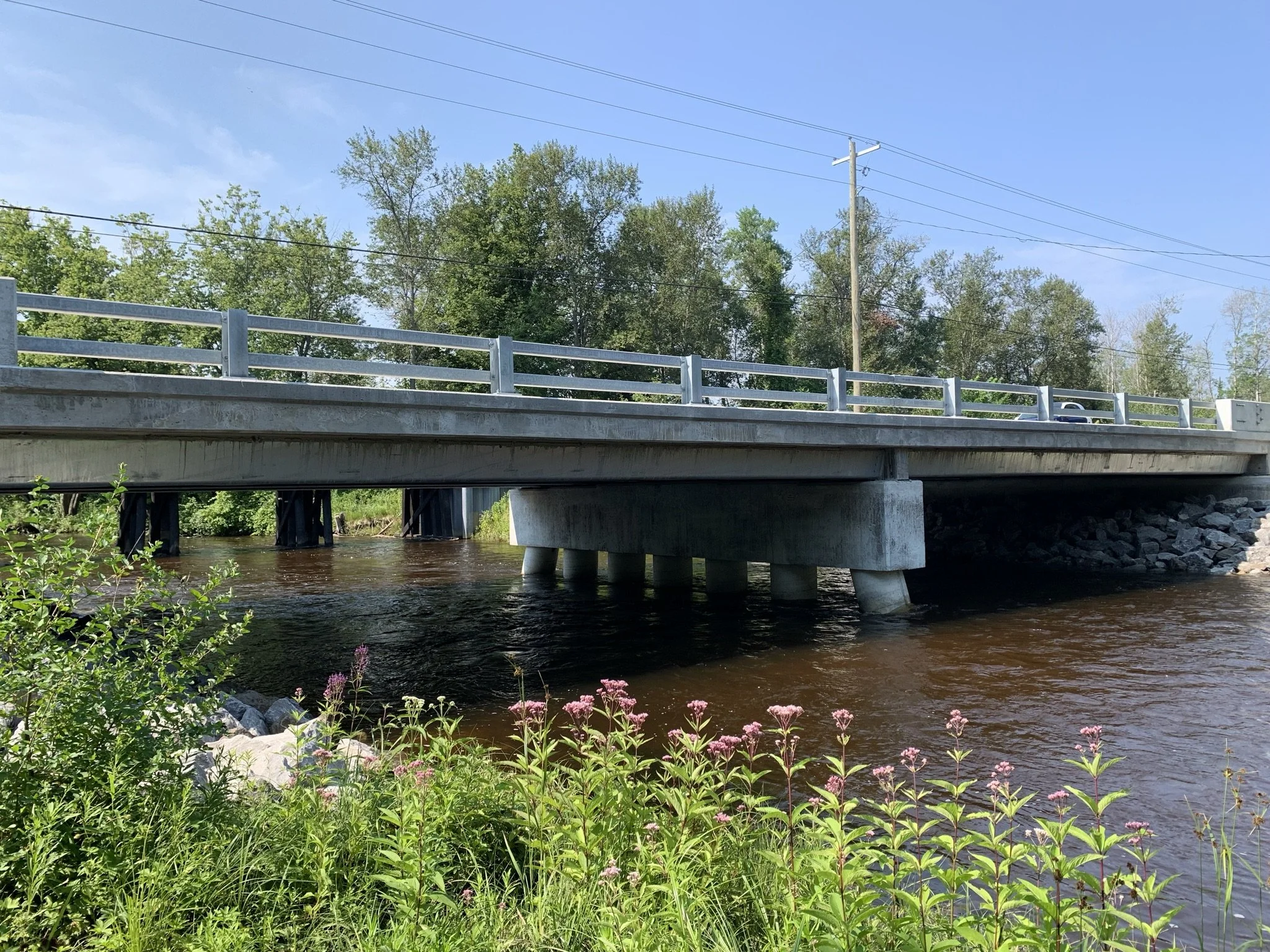 A bridge over a river with trees in the background and power lines crossing the sky.
