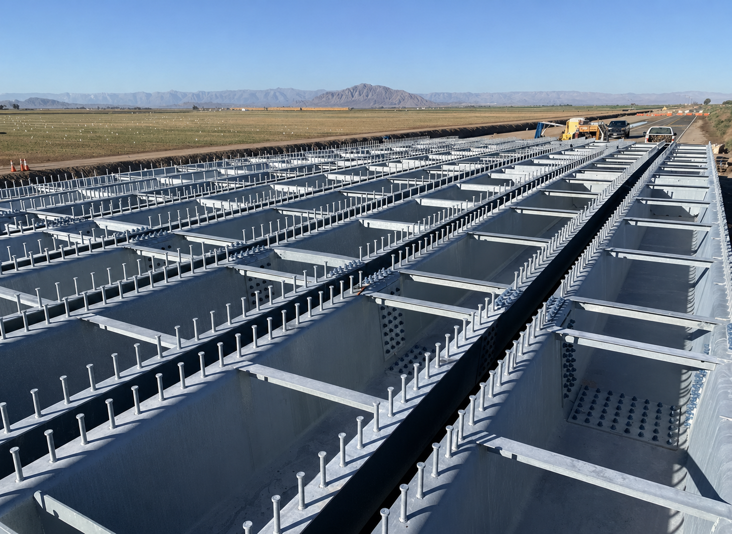 Construction of a large solar panel array outdoors with metal frames, bolts, and a blue sky, mountain range in the background.