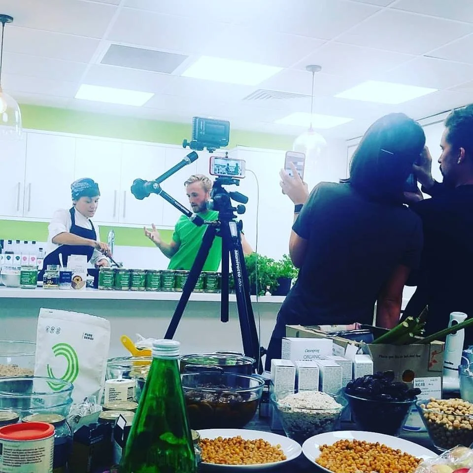 Filming a cooking show in a kitchen with multiple people, cameras, and food ingredients.