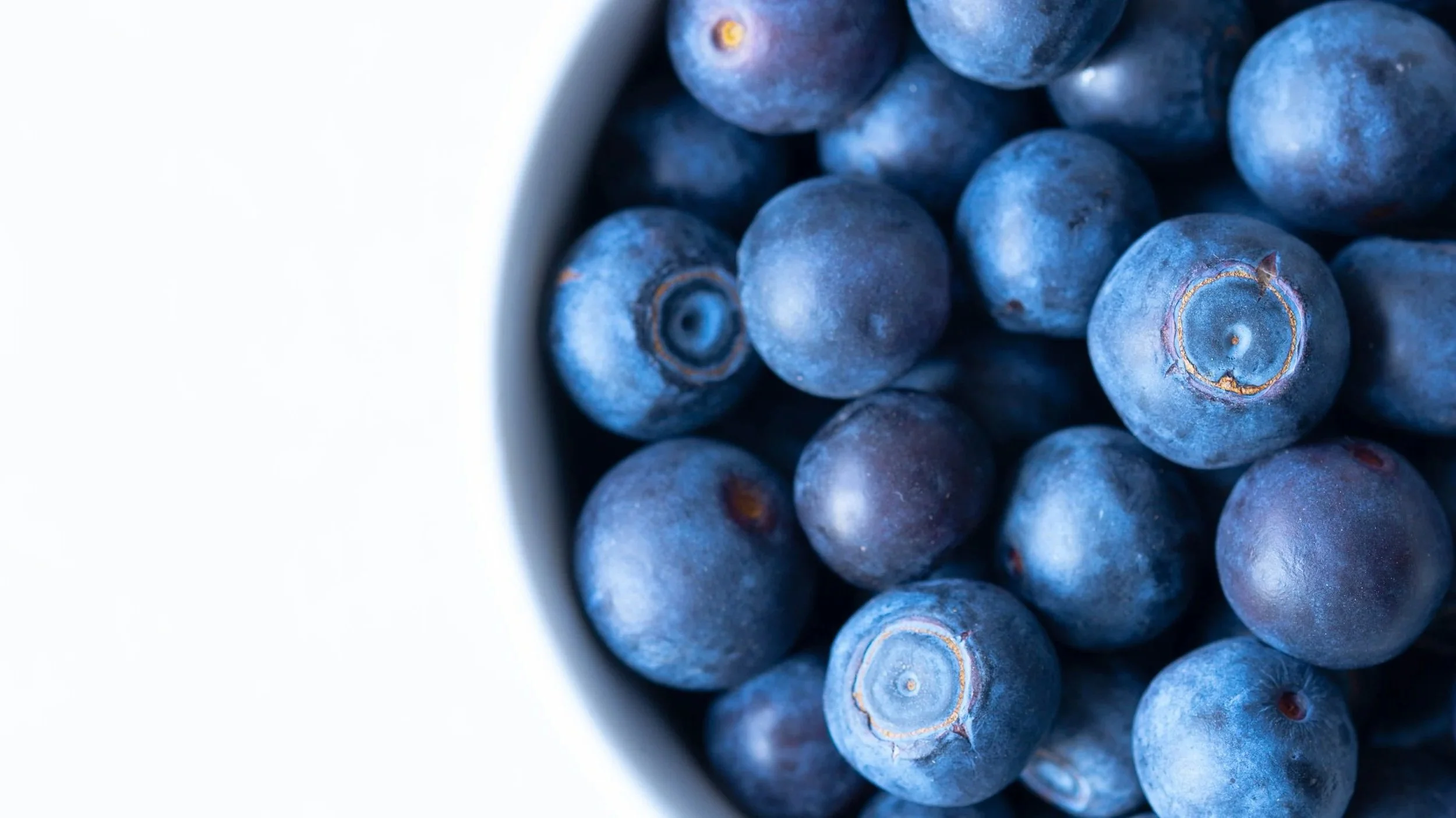 Close-up of fresh blueberries in a bowl on a white surface.
