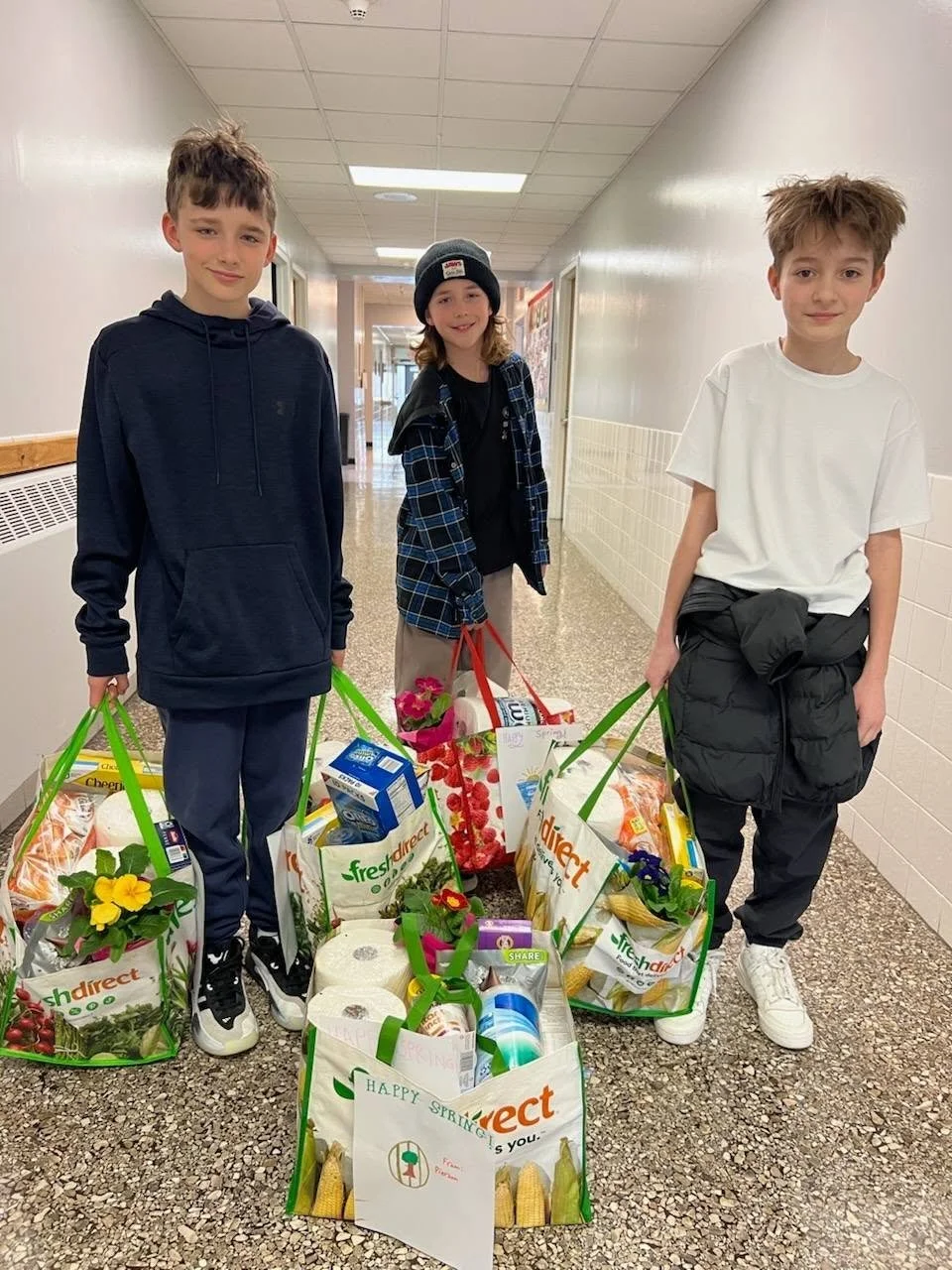 Volunteers standing in a hallway, each holding reusable shopping bags filled with groceries and flowers.