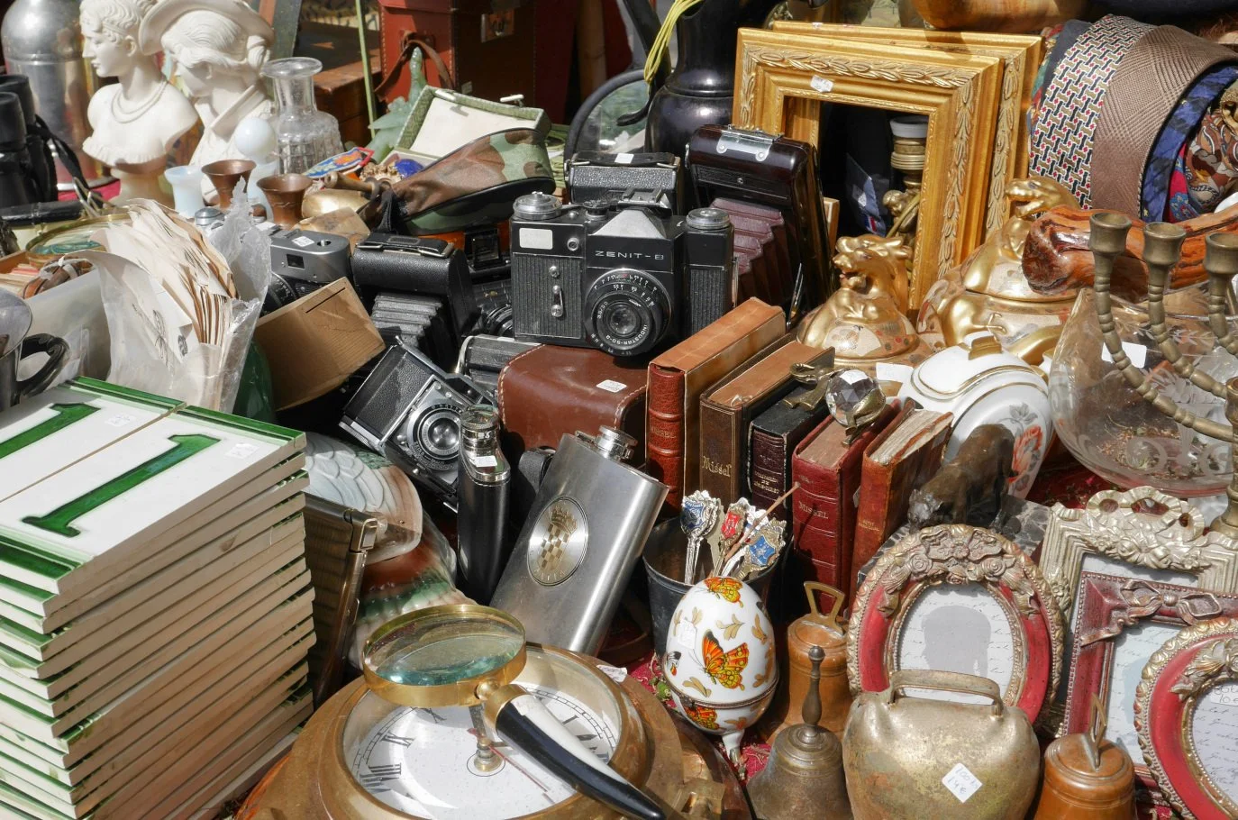A large assortment of vintage and antique items including cameras, books, picture frames, decorative glassware, flowers, and other collectibles at a flea market or thrift store.