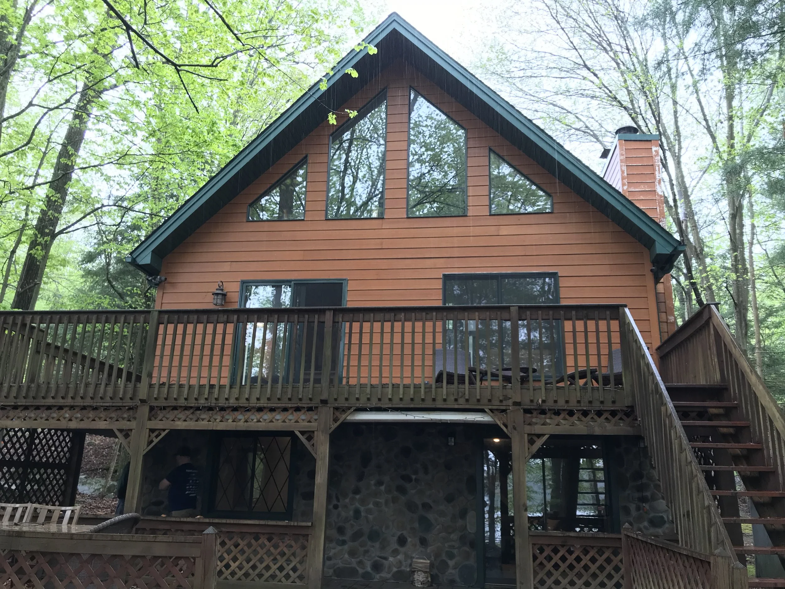 A multi-story house with a sloped roof, large windows, and a wooden deck in a wooded area.