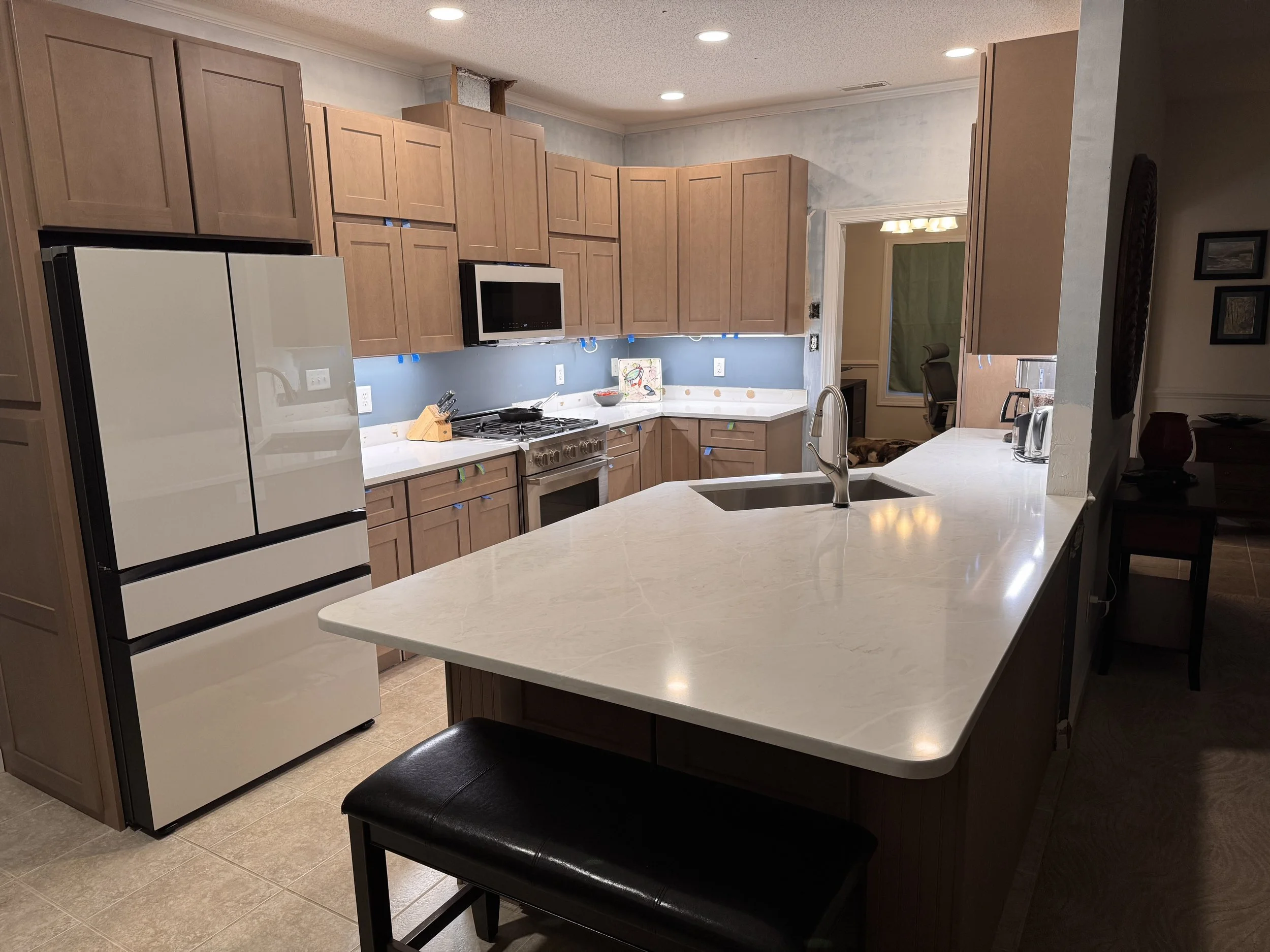 Modern kitchen with wooden cabinets, white countertop, stainless steel sink, black stovetop, microwave, and refrigerator.