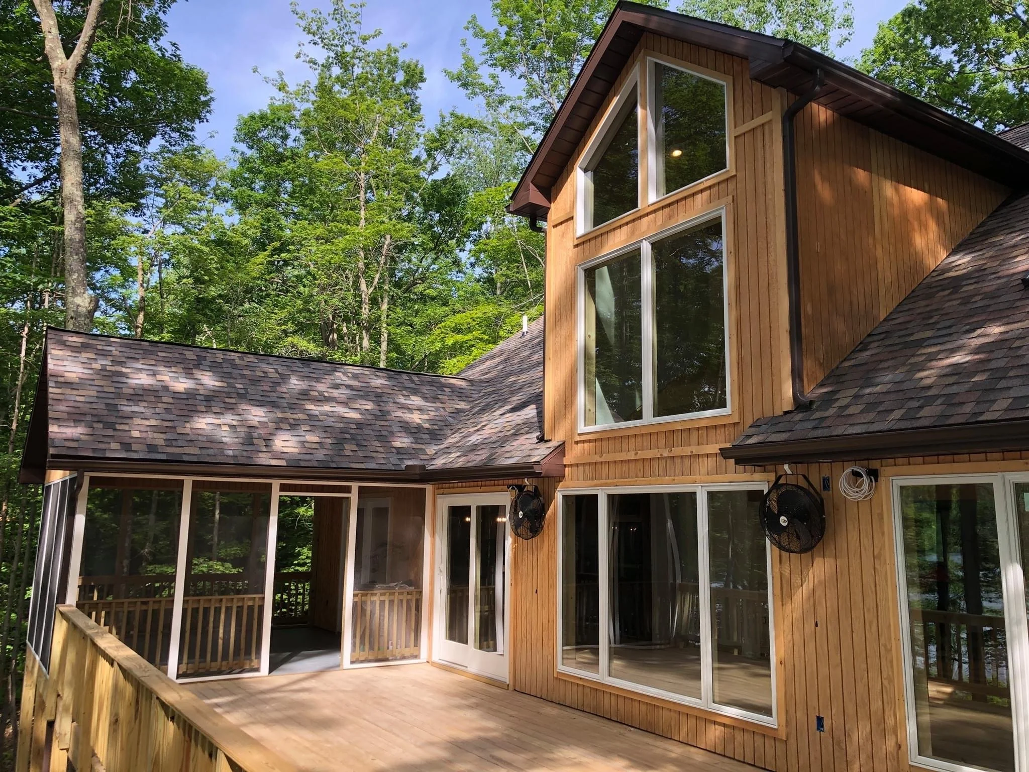A wooden house with large windows and a screened porch, surrounded by trees.