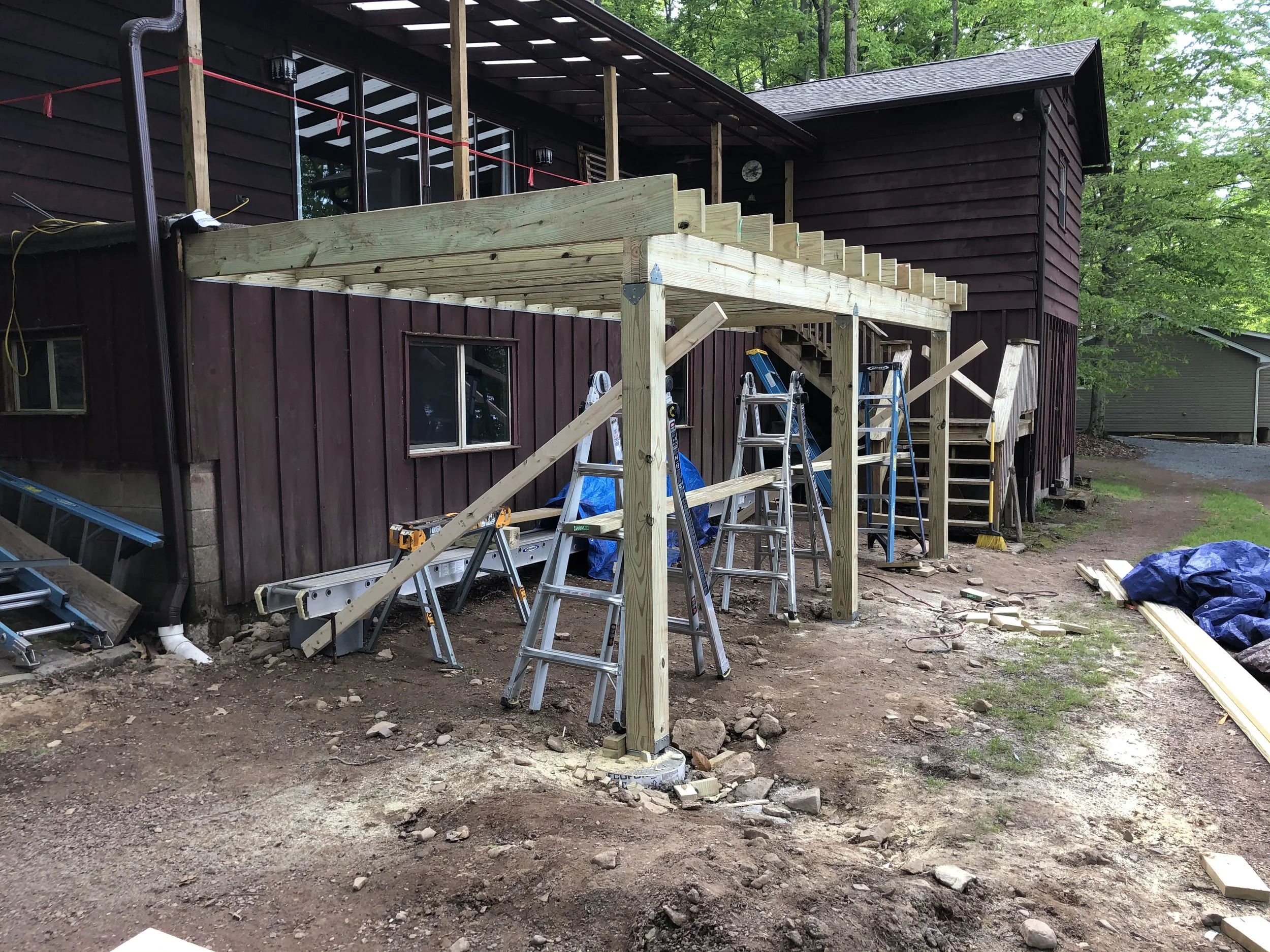 Wooden deck construction in progress on the back of a house with ladders and tools around.
