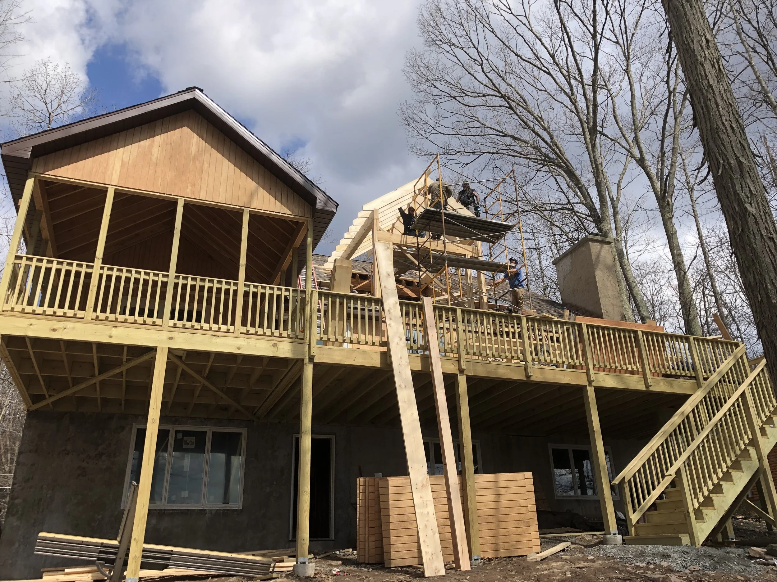 Construction workers building a multi-story wooden deck and house extension with scaffolding on a suburban house during daytime.
