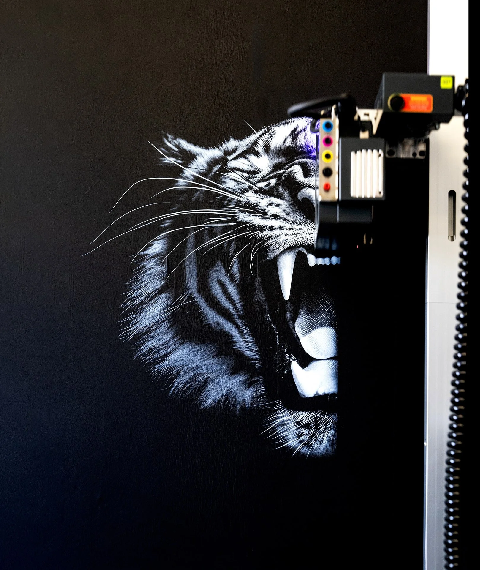 A black and white mural of a roaring tiger on a dark wall, partially obscured by a piece of electronic equipment.