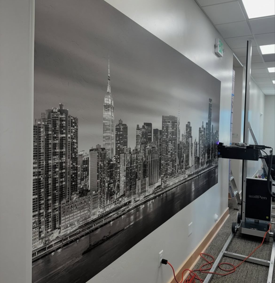 Black and white mural of New York City skyline including the Empire State Building, on an interior office wall, with a projector setup nearby.
