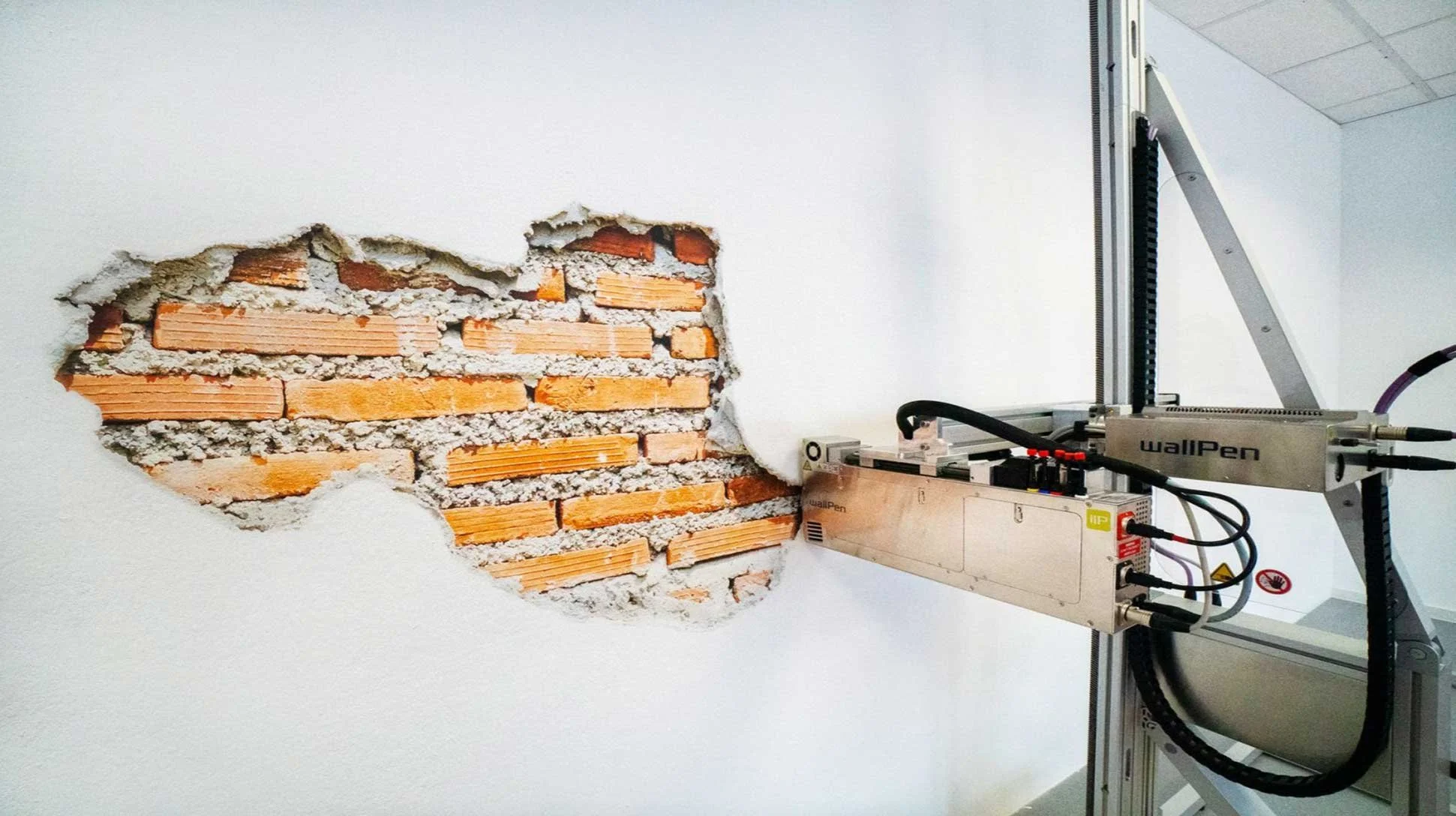 A robotic arm breaking through a white wall, revealing red bricks behind it.