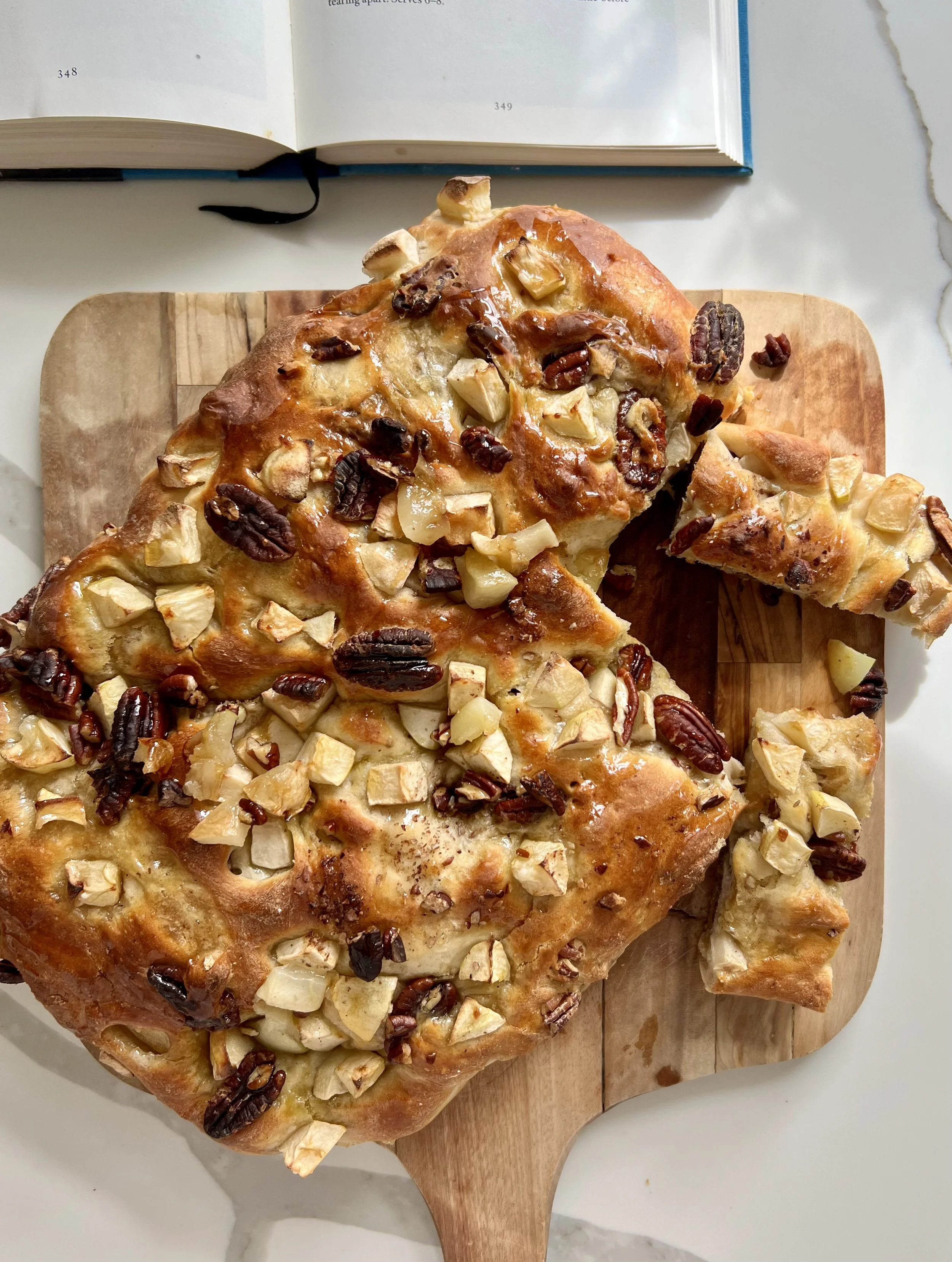 Close-up of a pecan and apple tart on a wooden serving board, with an open book in the background.