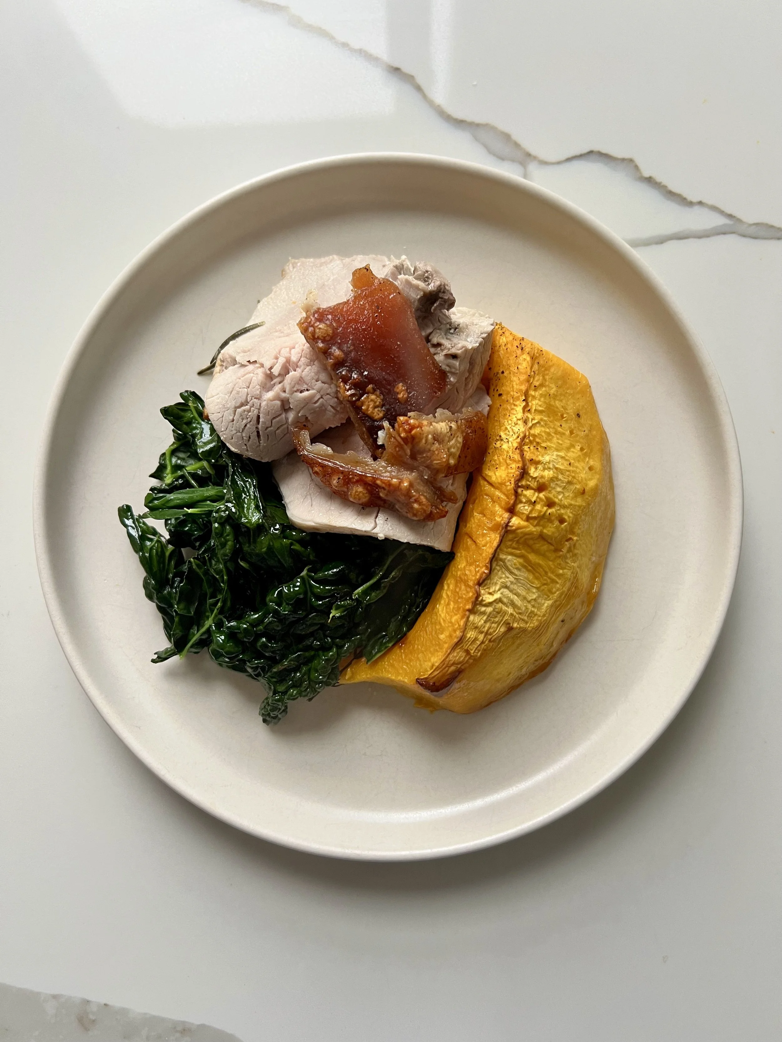 A white plate with cooked spinach, sliced cooked turkey with gravy, roasted pumpkin wedge, and a piece of glazed bacon.