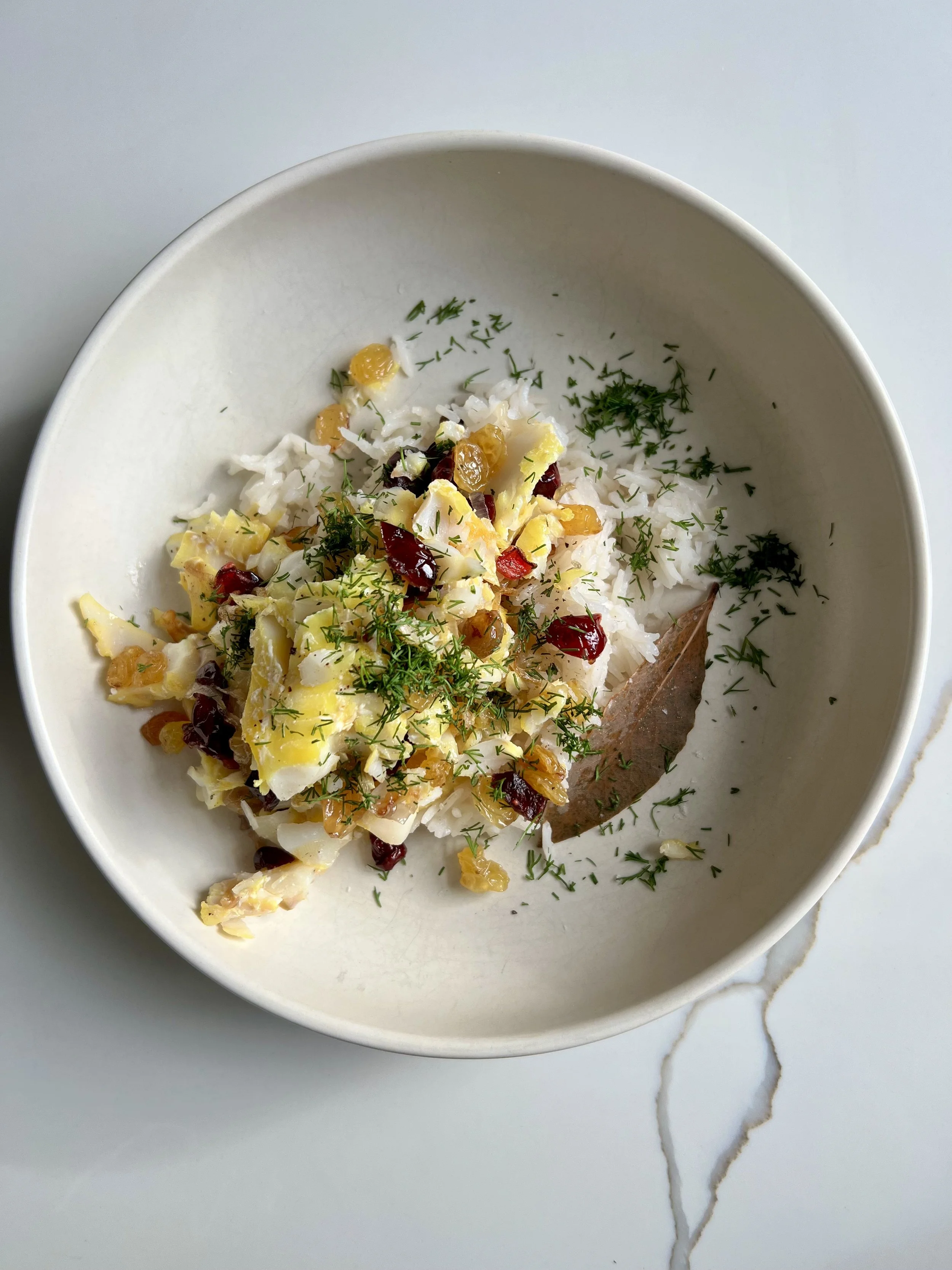 A white bowl filled with cooked white rice topped with chopped boiled eggs, red peppers, herbs, and sprinkled with green herbs, placed on a light-colored surface with a marble pattern.