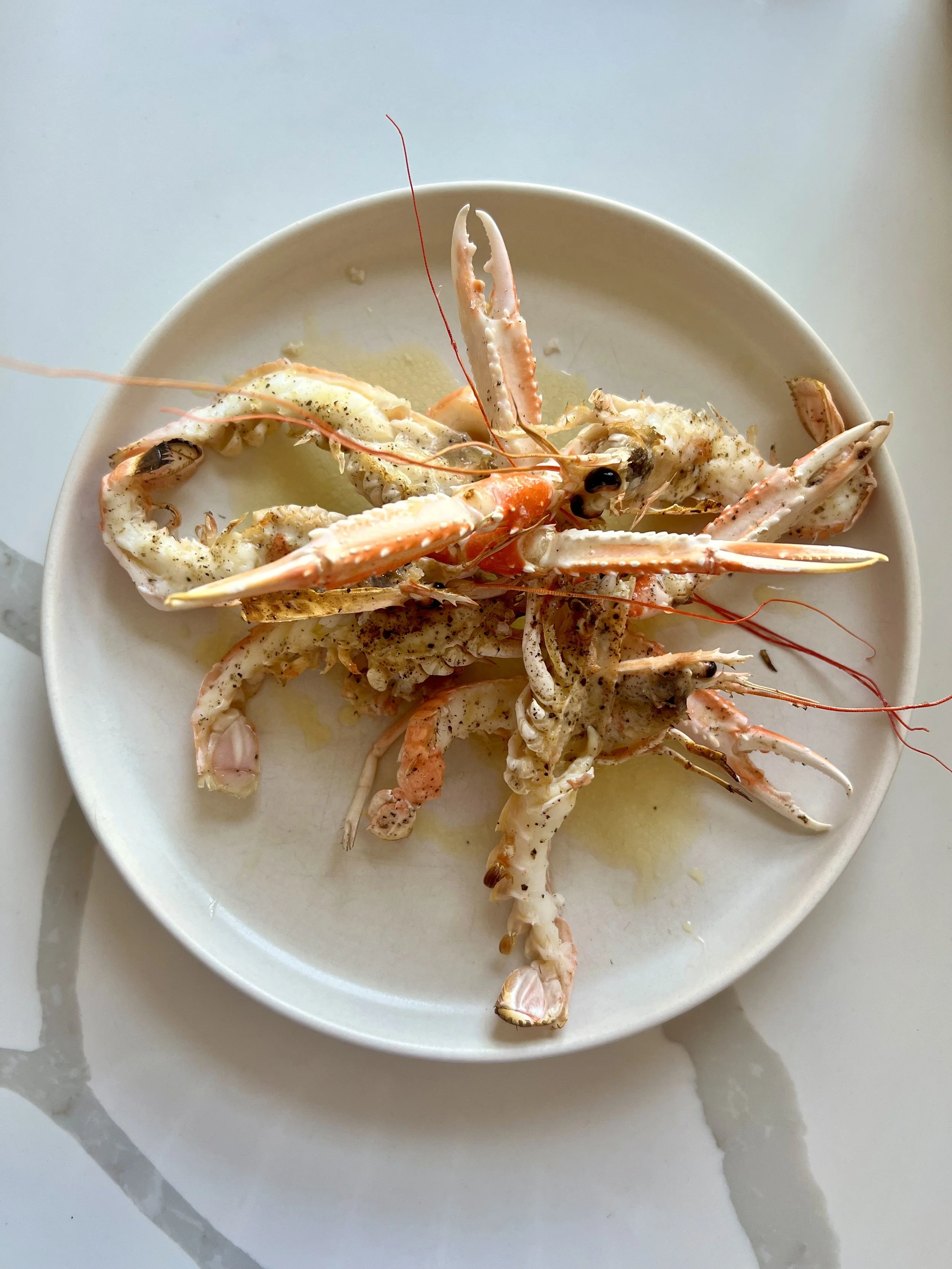 A white bowl containing cooked lobster tails with black pepper and butter.