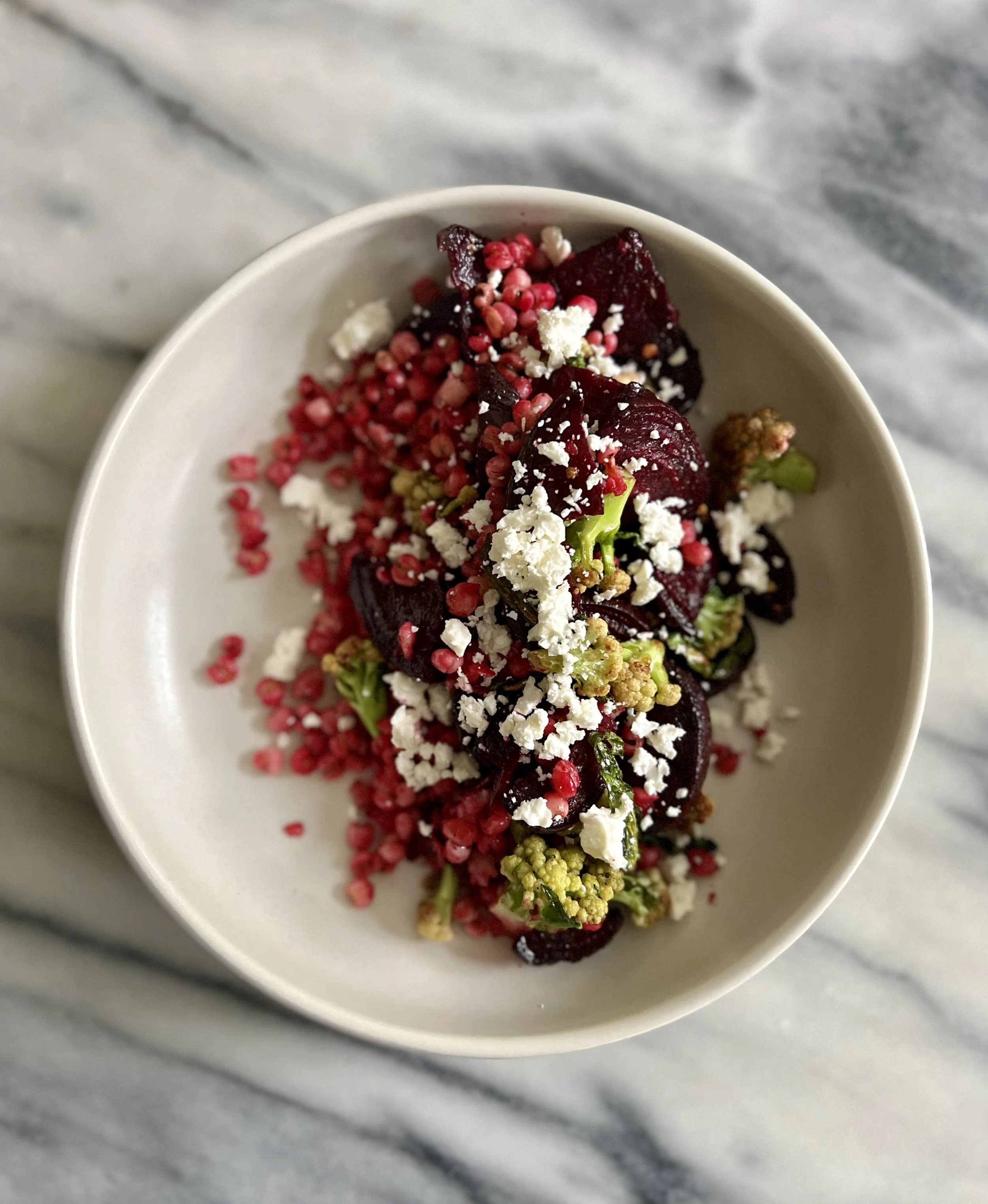 A close-up view of a bowl of mixed berries and granular toppings on a gray marble surface.