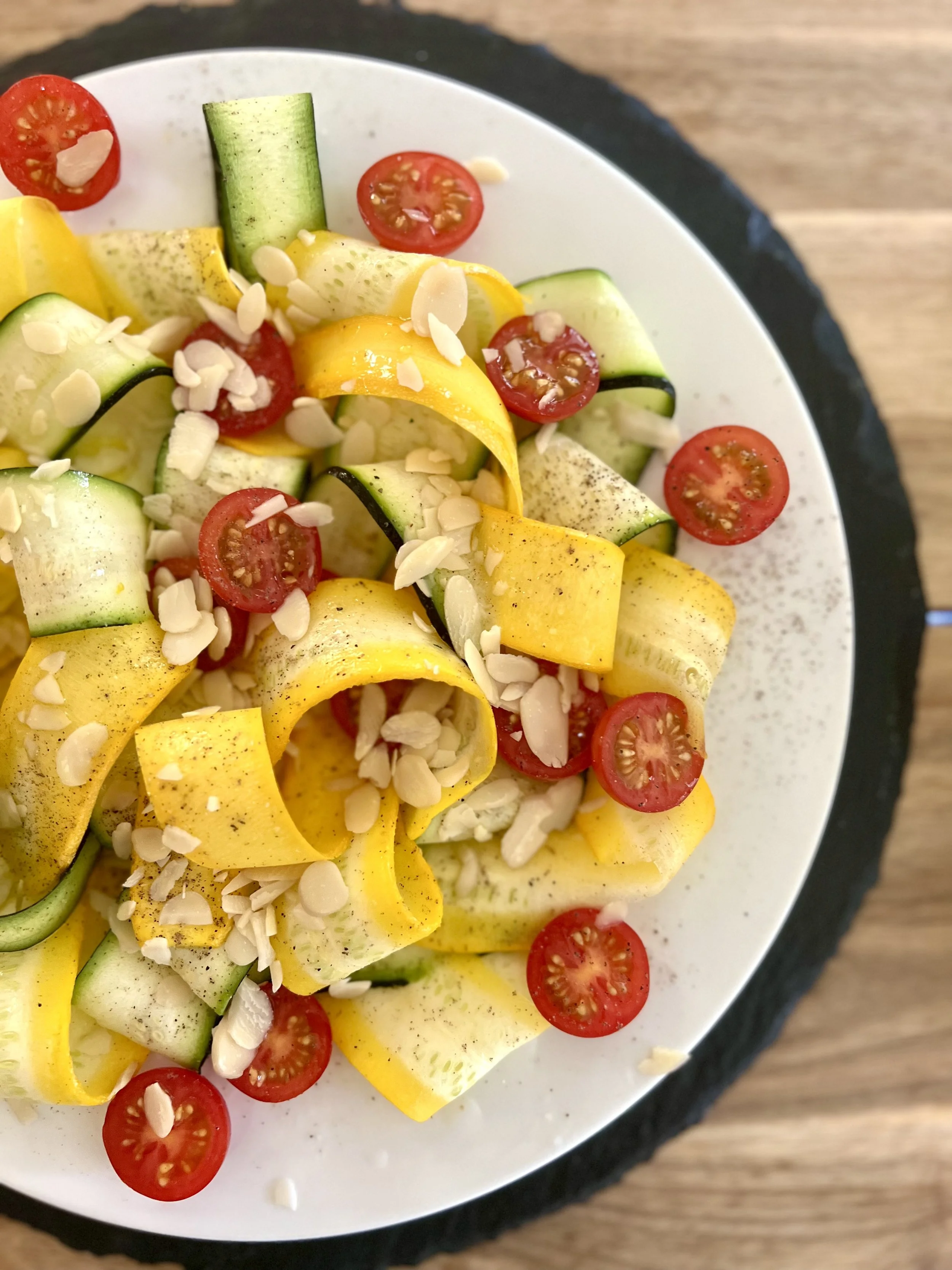 Slice of cucumber, cherry tomatoes, yellow squash, sliced almonds, and pepper on a white plate.