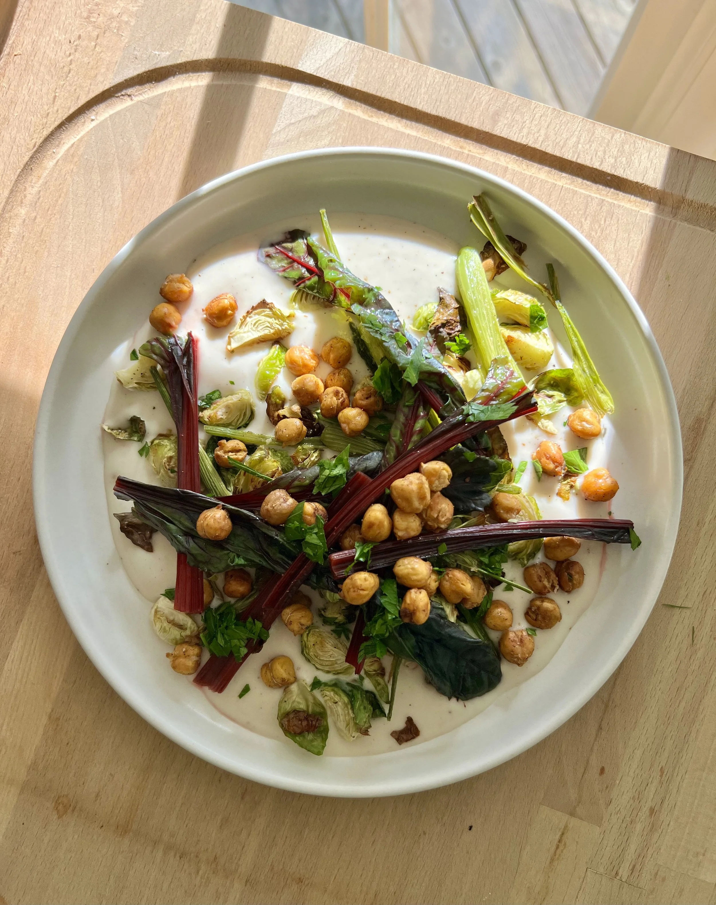 A white oval plate filled with salad, including chickpeas, mixed greens, and a creamy dressing, placed on a wooden table.