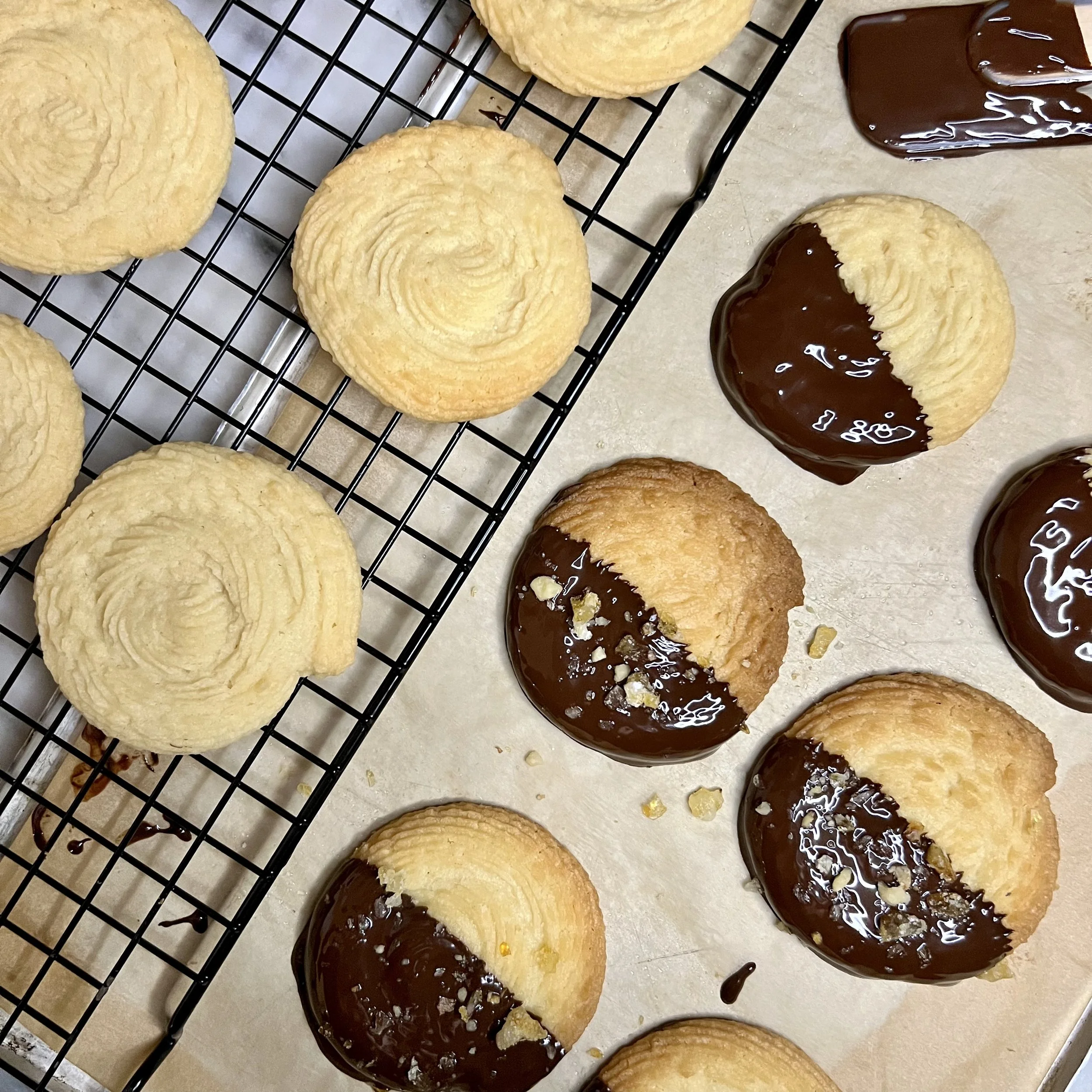 Cookies with chocolate coating and chopped nuts on top, cooling on a wire rack and a baking sheet.