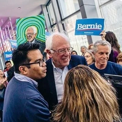Bernie Sanders and Sam Sukaton smiling and talking with supporters at a campaign event.