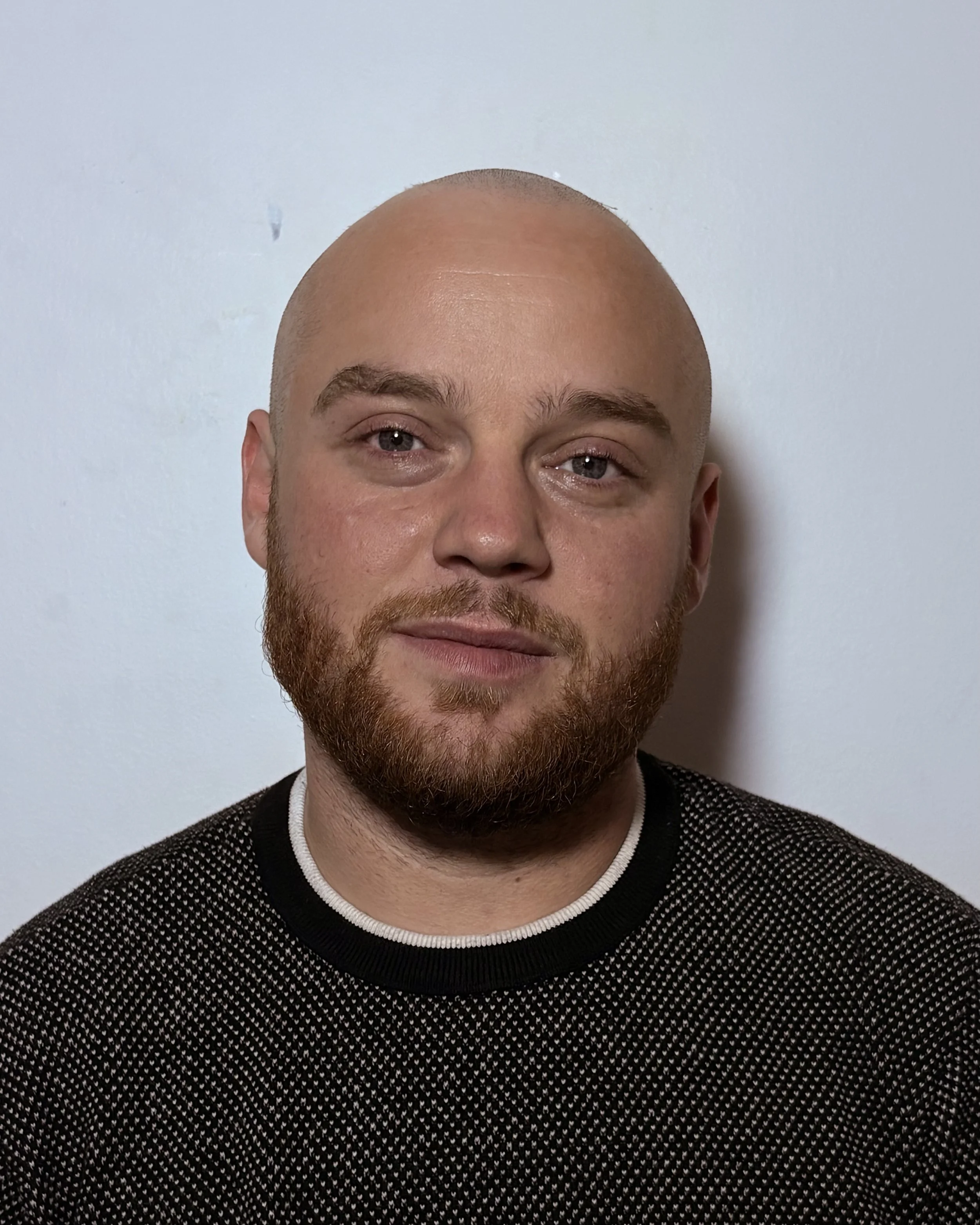 A man with a shaved head and a beard looking at the camera.