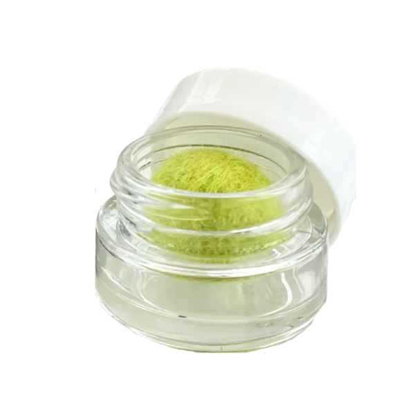Open clear plastic container with a greenish-yellow sponge applicator inside, partially unscrewed lid resting on the side.