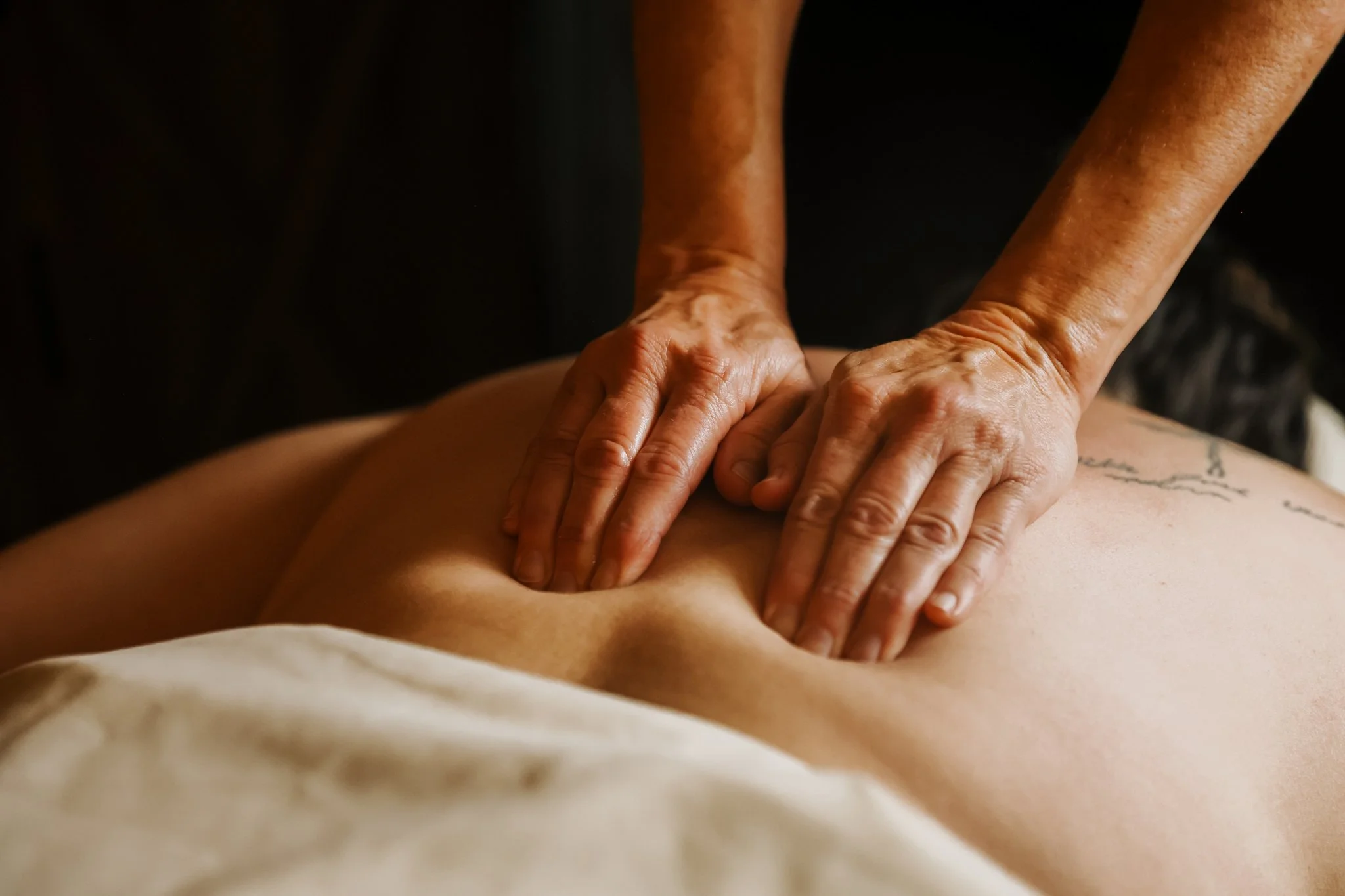 Close-up of a person receiving a massage on their back from a massage therapist, with focus on the therapist's hands pressing into the skin.