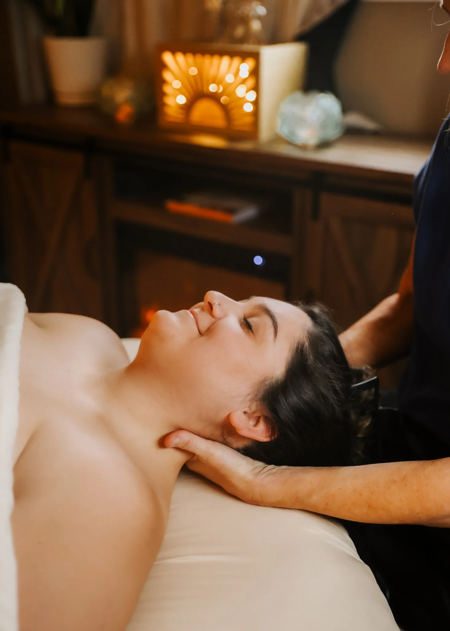 A woman receiving a relaxing massage in a cozy room with warm lighting and wooden furniture.
