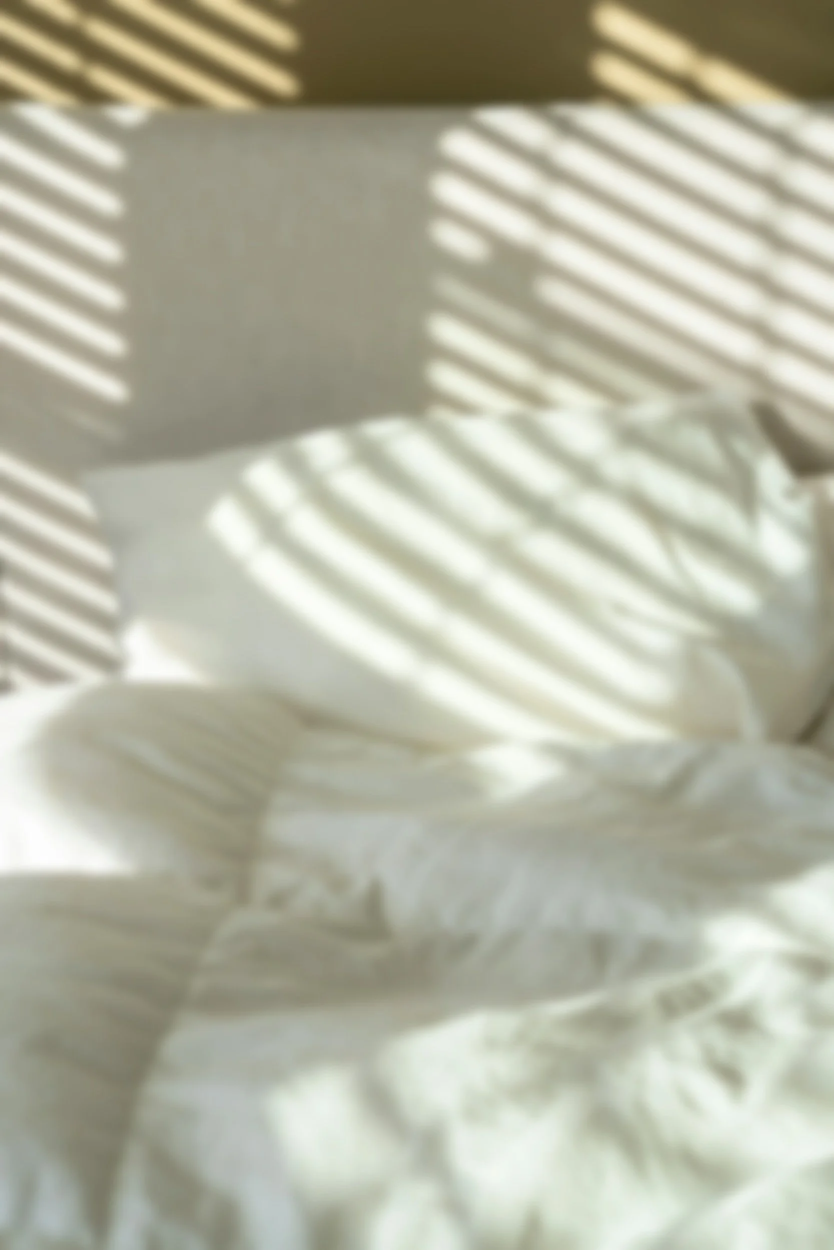 Sunlight casting striped shadows on a white bed with pillows.