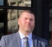 A man wearing a suit standing outdoors near a building with glass windows