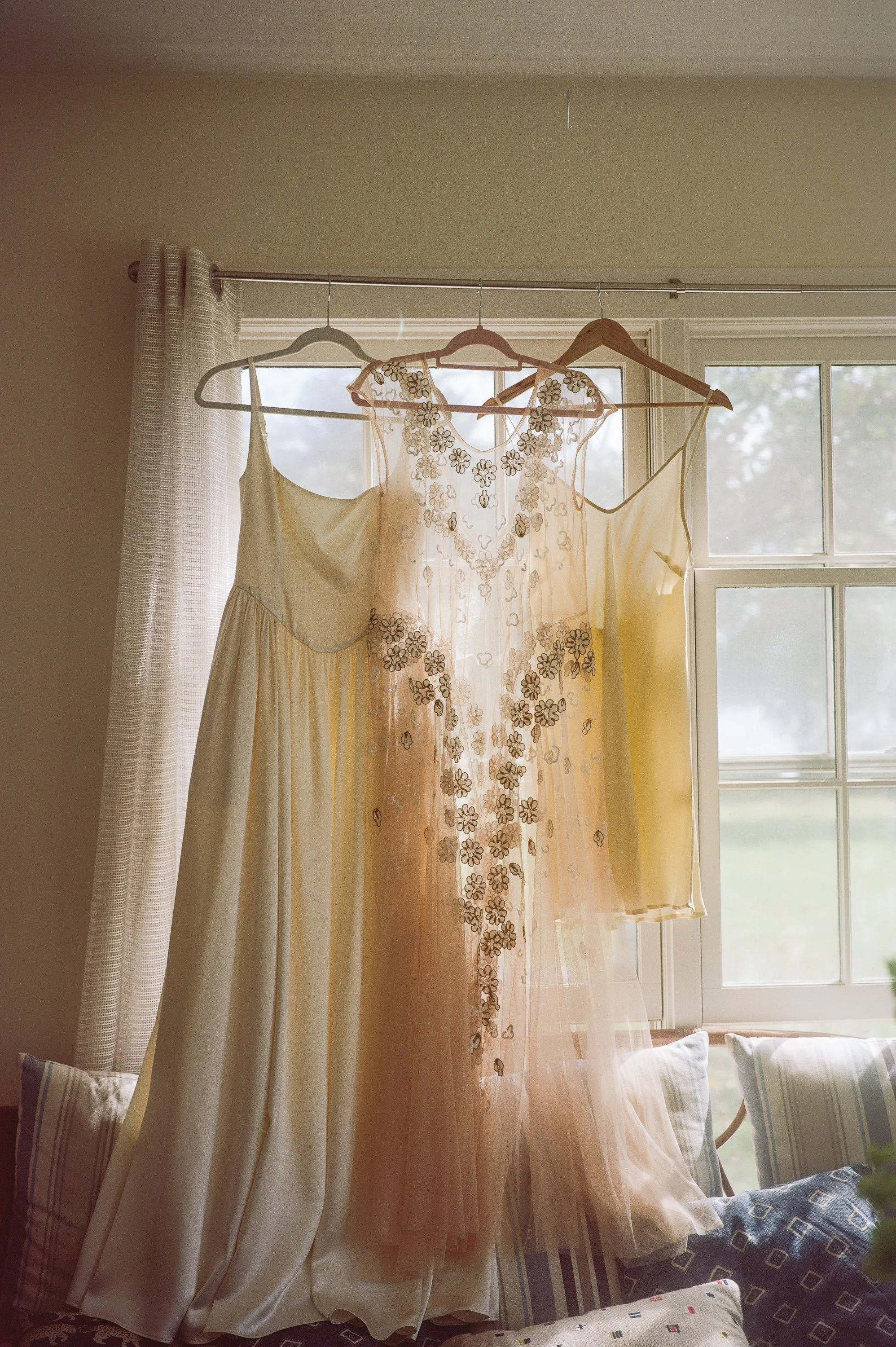 A timeless bridal getting-ready moment captured on film, featuring a bride gently holding her wedding dress in soft natural light. Fine-art wedding photography documenting the quiet, intimate moments before the ceremony with a romantic, nostalgic, an