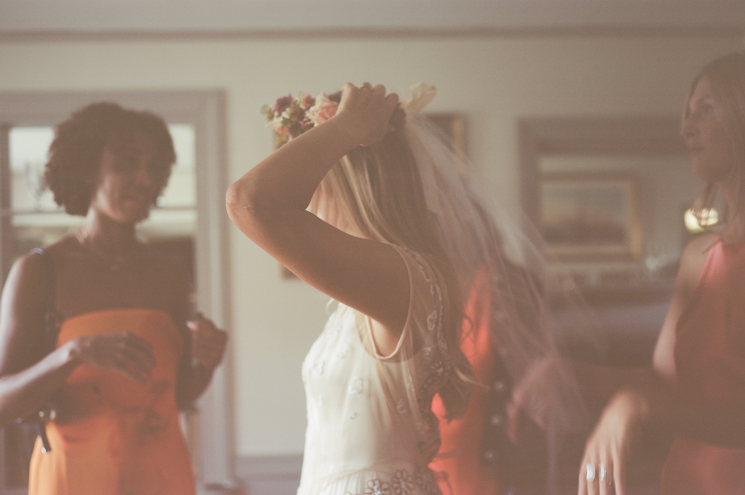 A romantic bridal portrait of a bride adjusting her wedding veil, captured on film with soft natural light and timeless editorial styling. Fine-art wedding photography preserving the quiet, intimate getting-ready moments with a nostalgic, documentary
