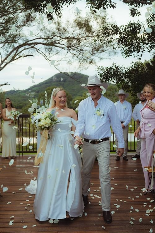 Newly married couple walk down aisle hand in hand through petal toss at Yandina Station