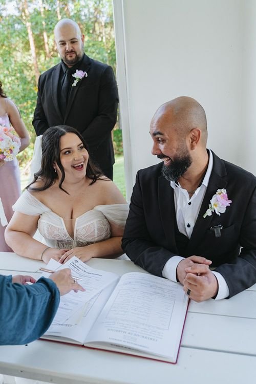 Excited newlywed couples sit at signing table going through Marriage Certificates
