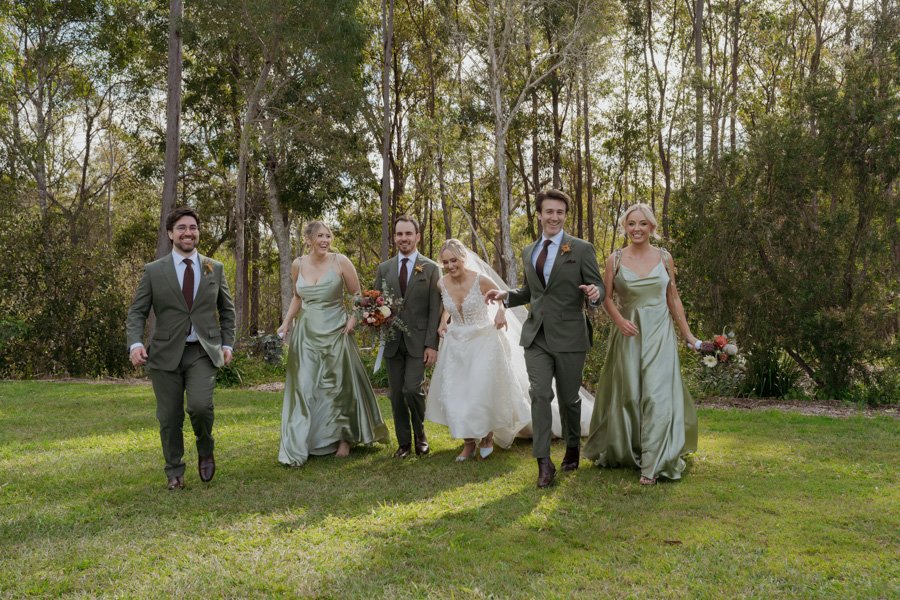 Bridal party having fun running towards camera in park