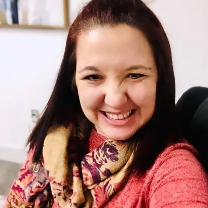 A woman smiling and taking a selfie indoors with a microphone nearby.