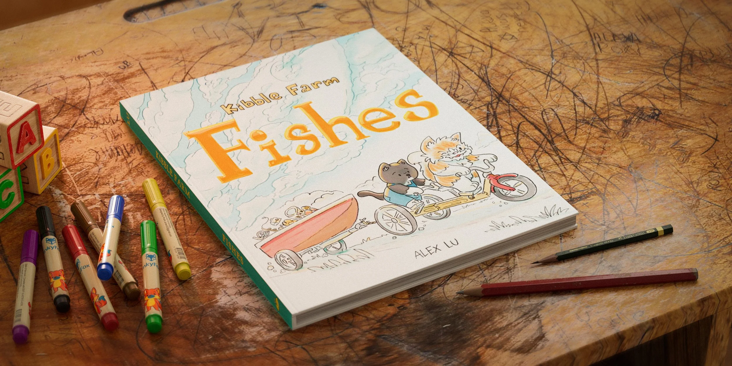 A children's coloring book titled 'Kyble Farm Fishes' with a drawing of two animated animals riding a bicycle on a table, surrounded by colored markers and wooden alphabet blocks.