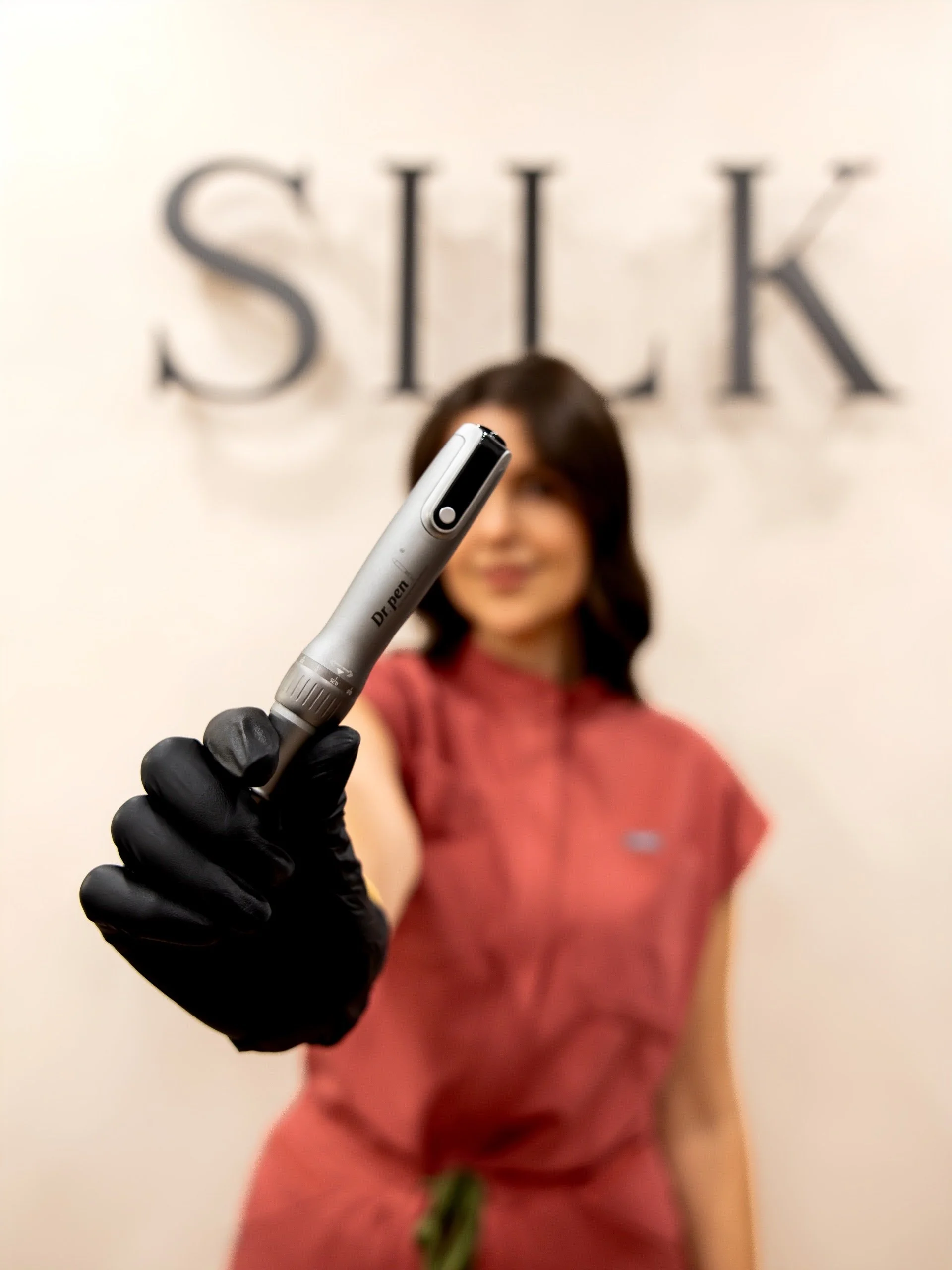 Aesthetician in gloves holding a Dr. Pen microneedling device in a skincare clinic