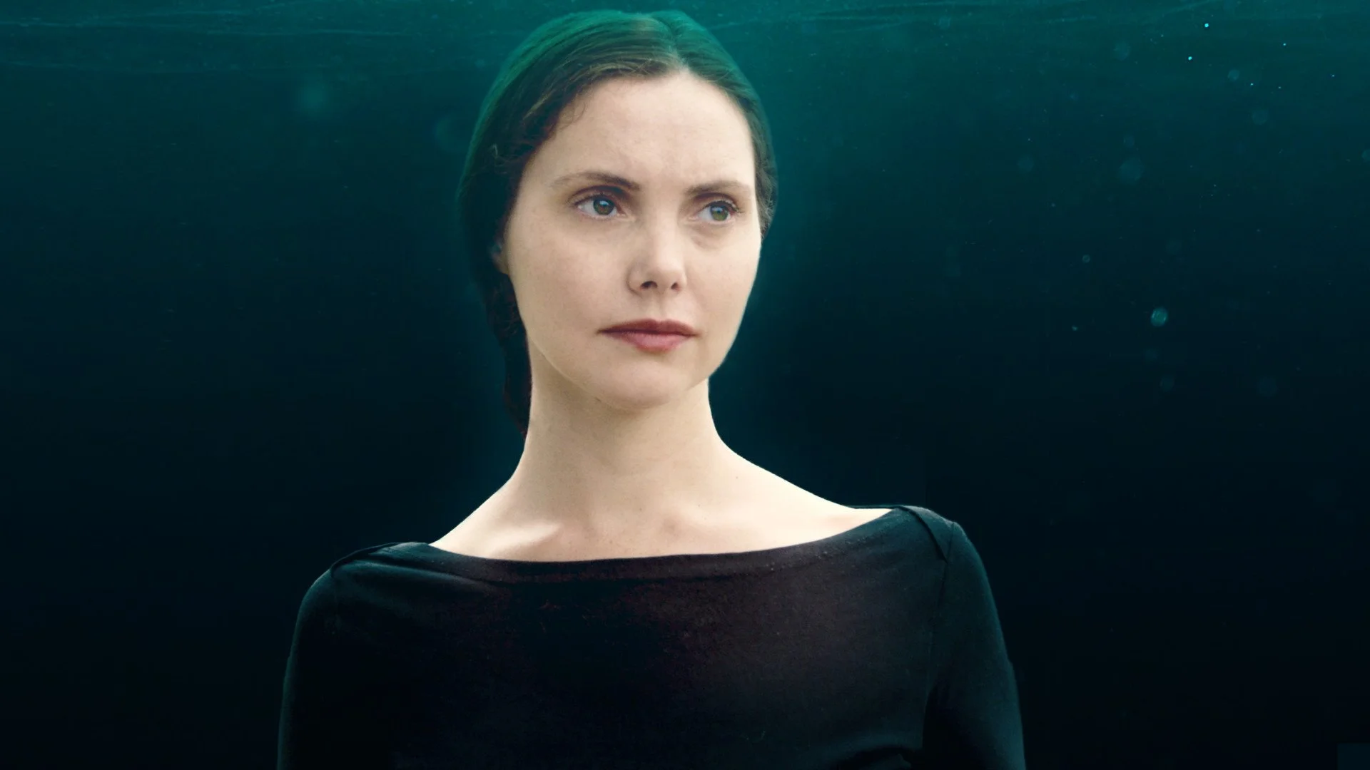 A woman with short dark hair, wearing a black top, underwater with a dark background.