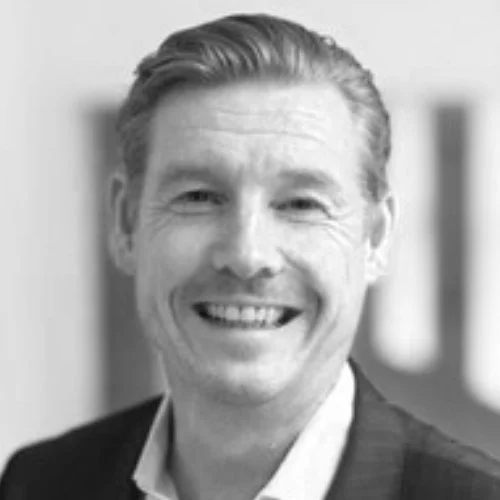 Black and white portrait of a man smiling in a suit and collared shirt.