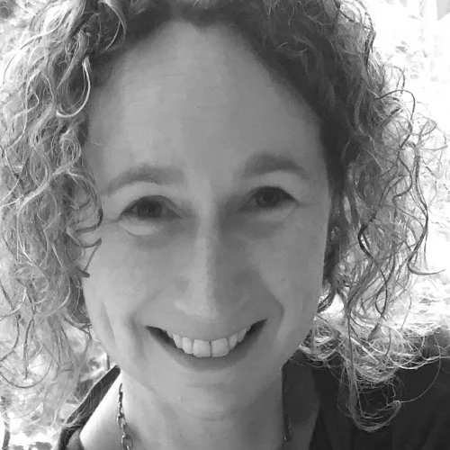 Close-up of a smiling woman with curly hair and light skin, looking at the camera.