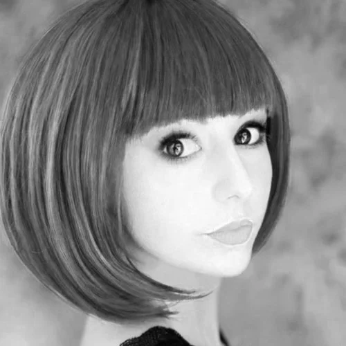 Black and white portrait of a woman with a short, straight bob haircut and bangs, looking at the camera with a neutral expression.