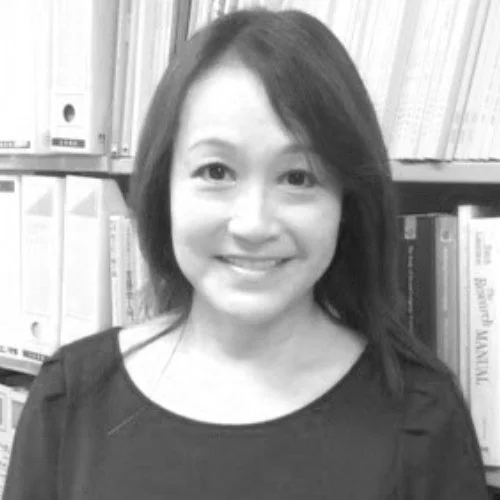 A woman with shoulder-length hair smiling in front of a bookshelf filled with books.