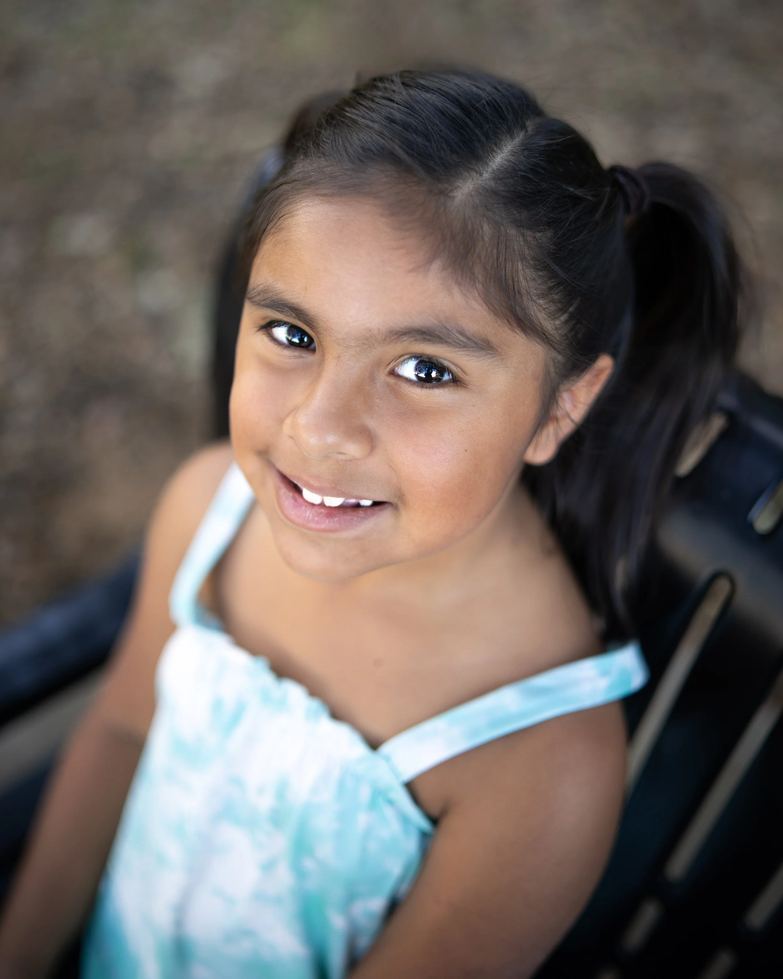 A young girl sitting on a park bench, smiling and looking up at the camera.